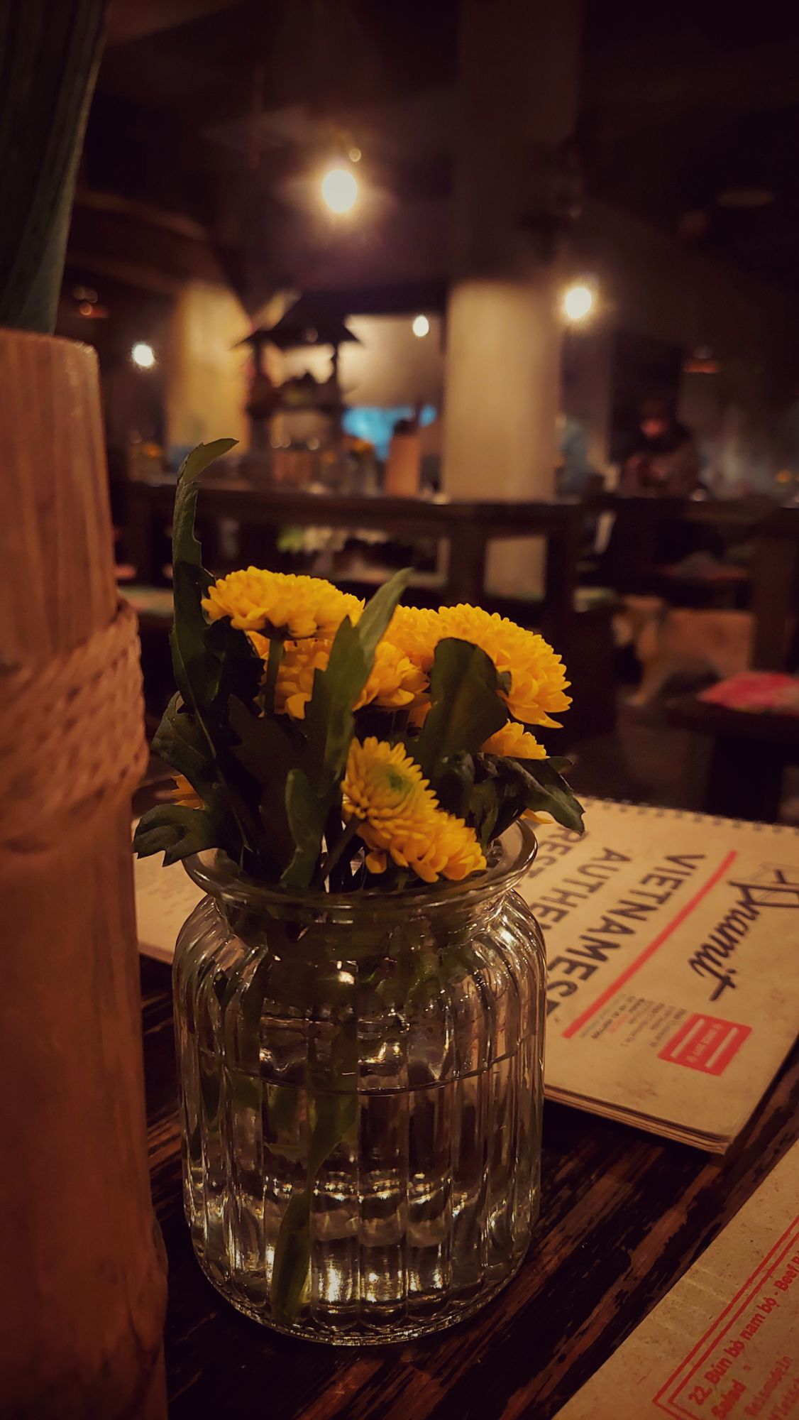 Table decoration in a restaurant: Flowers, a wooden vessel containing spoons, and a menu