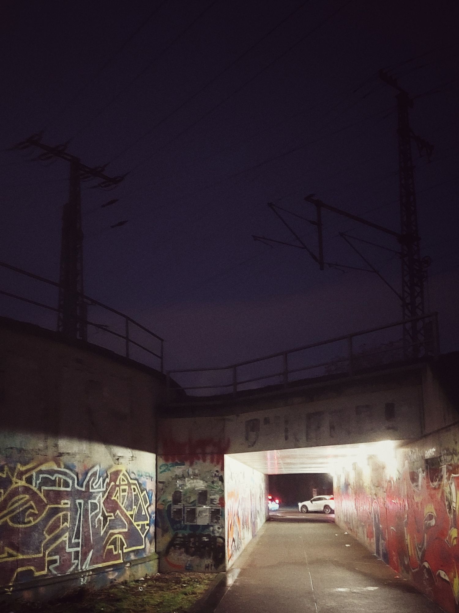 Stromlinien, Eisenbahnschienen, ein Fussgaengertunnel, graffitiverziert. Dahinter Autos im Morgenstau.