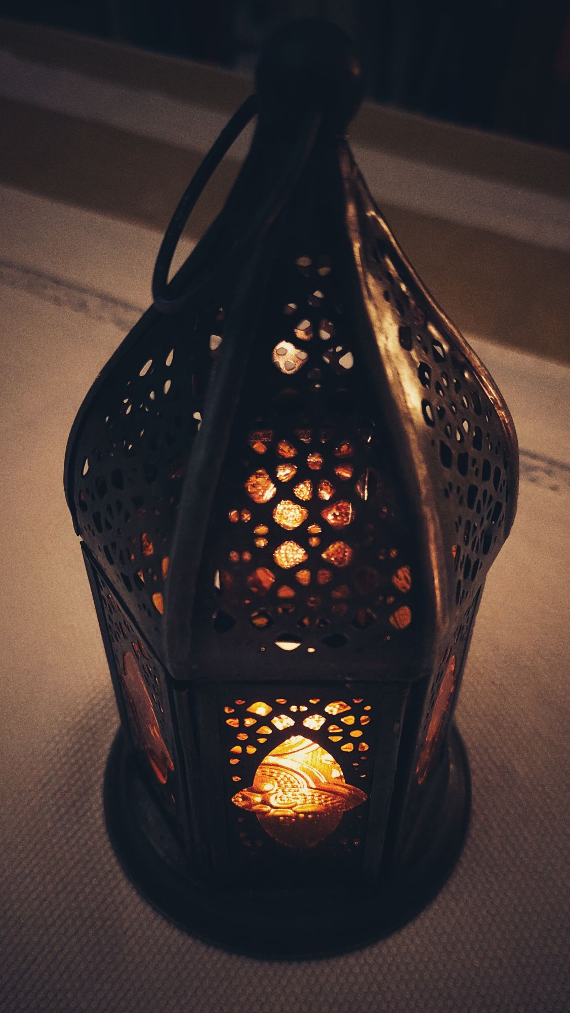 A small metal lantern with a small candle inside, placed on a tablecloth.