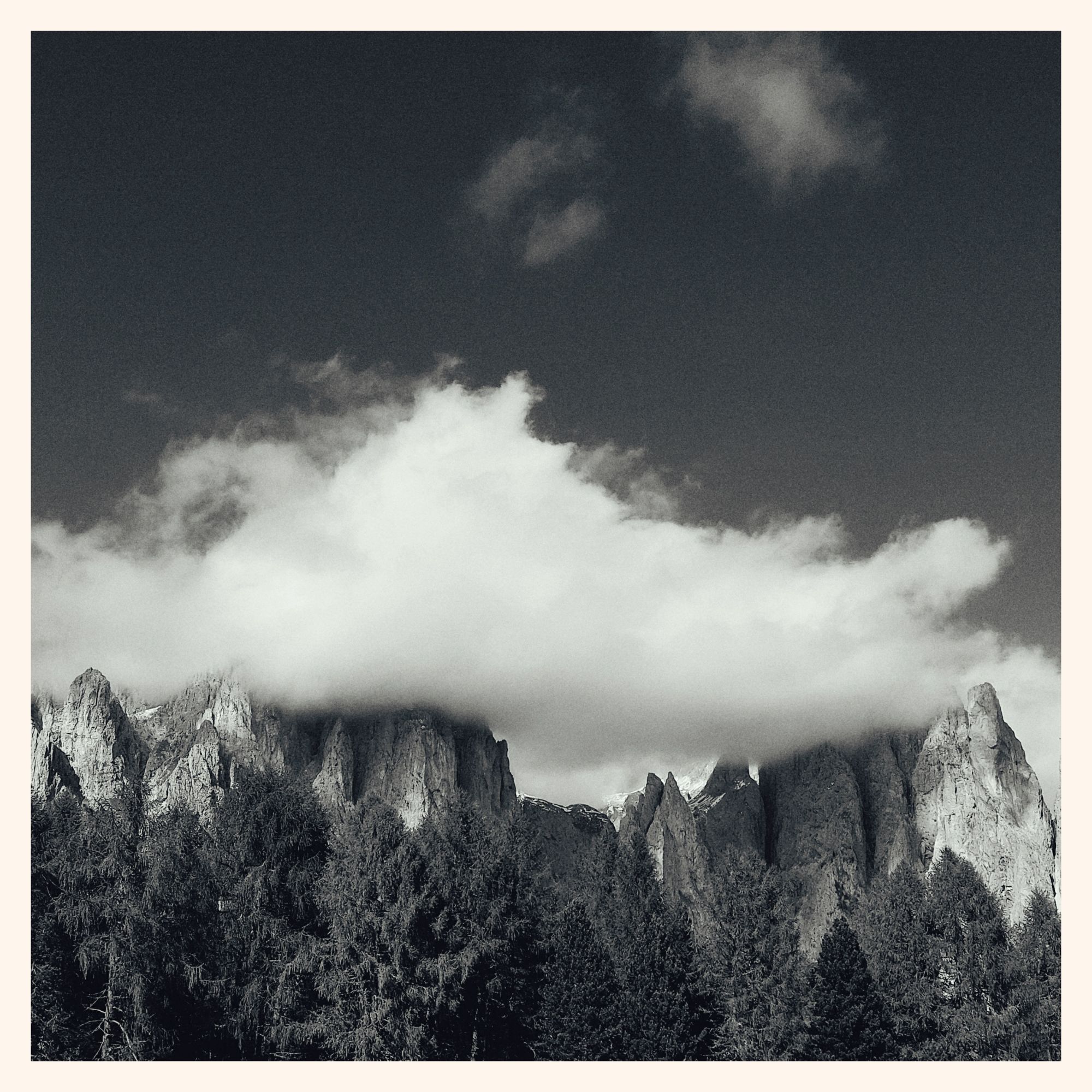 Monochrome shot of a huge white cloud resting on a mountain massif. 