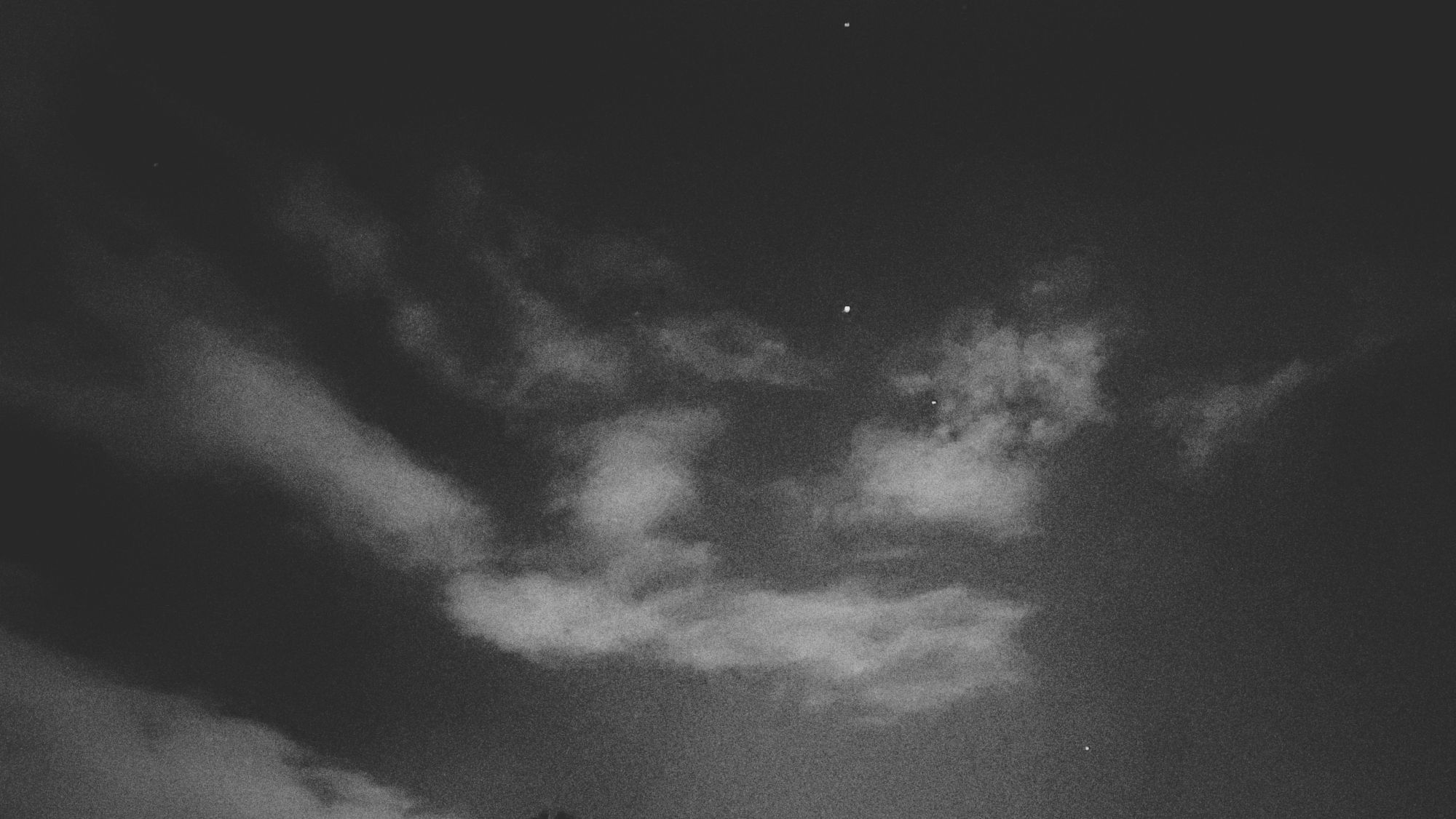Monochrome grainy shot. Clouds on a late evening sky. Some bright spots in between. 