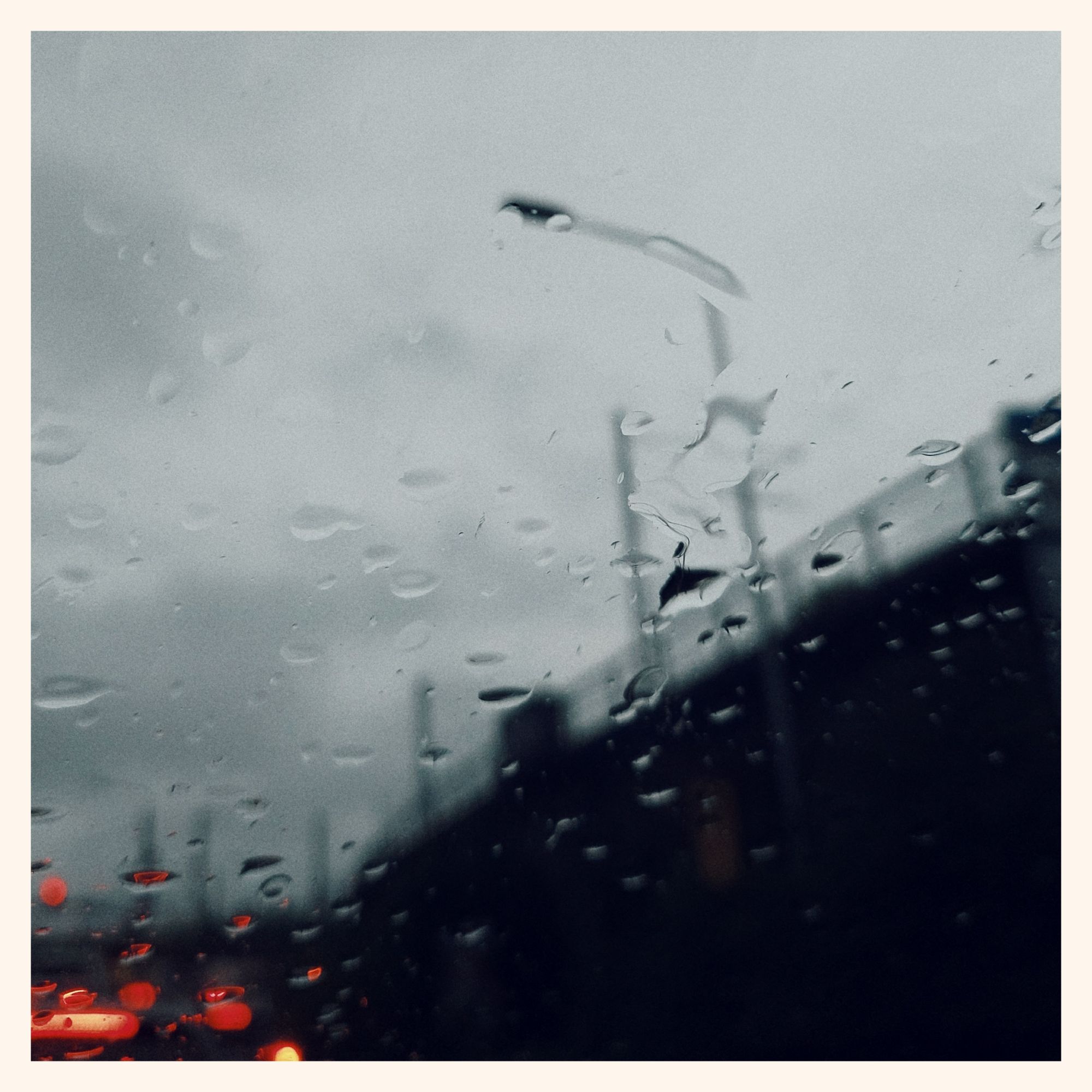 Raindrops on a windowpane. Grey sky, railroad infrastructure and cars in a jam behind. Some red back-lights in the grey.