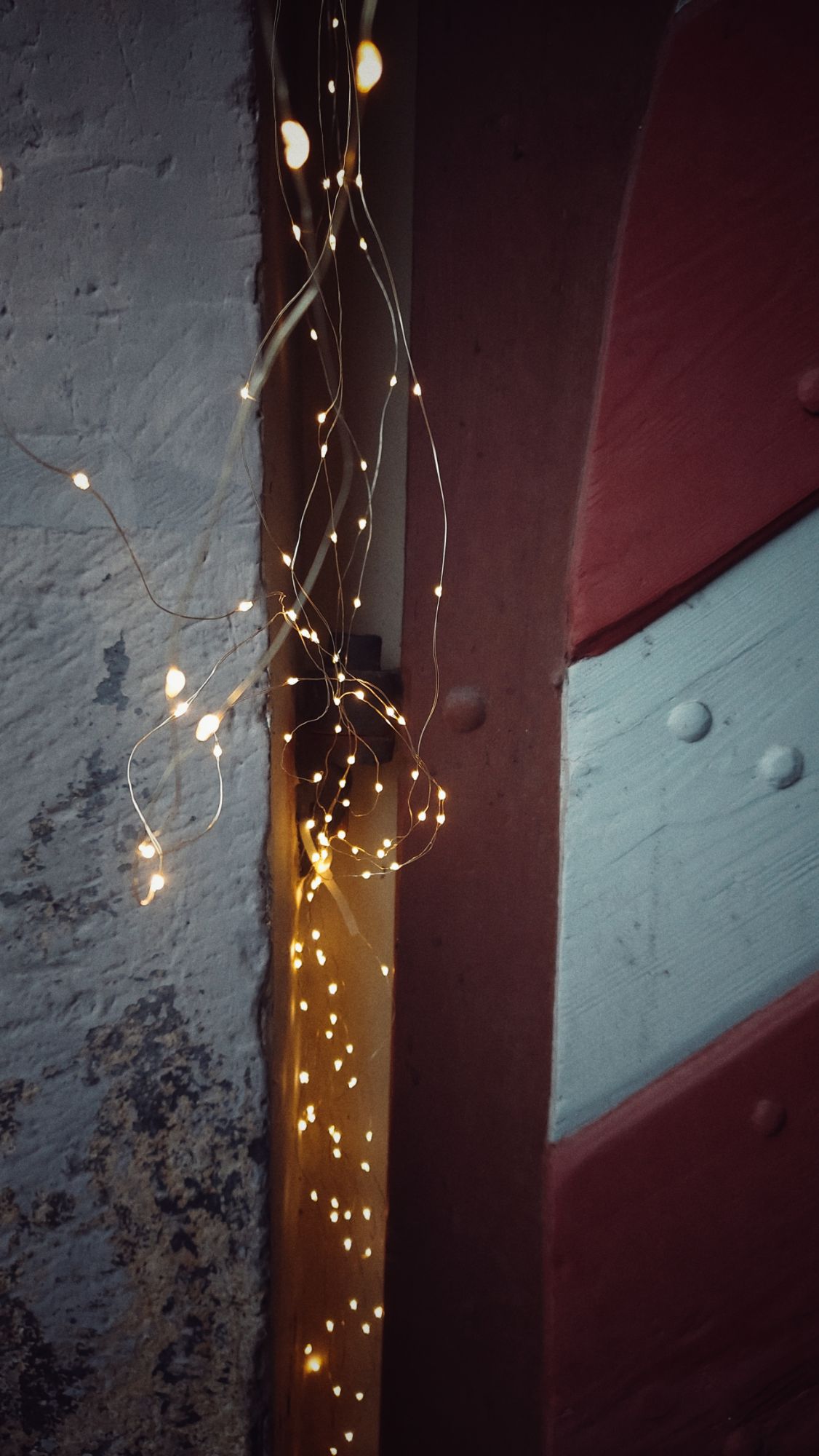 A chain of small lights hanging in between a wall and a red and white old door.