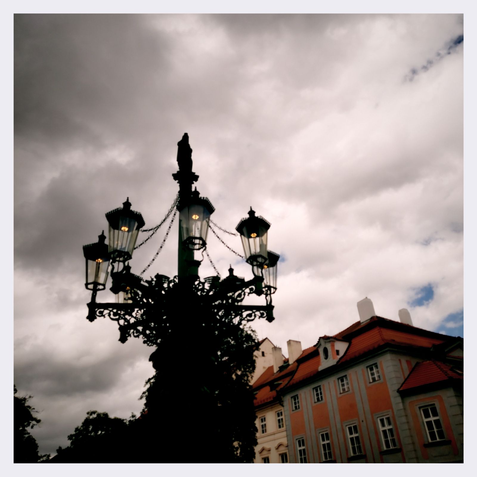A seven-flame public lantern, a house and grey clouds.