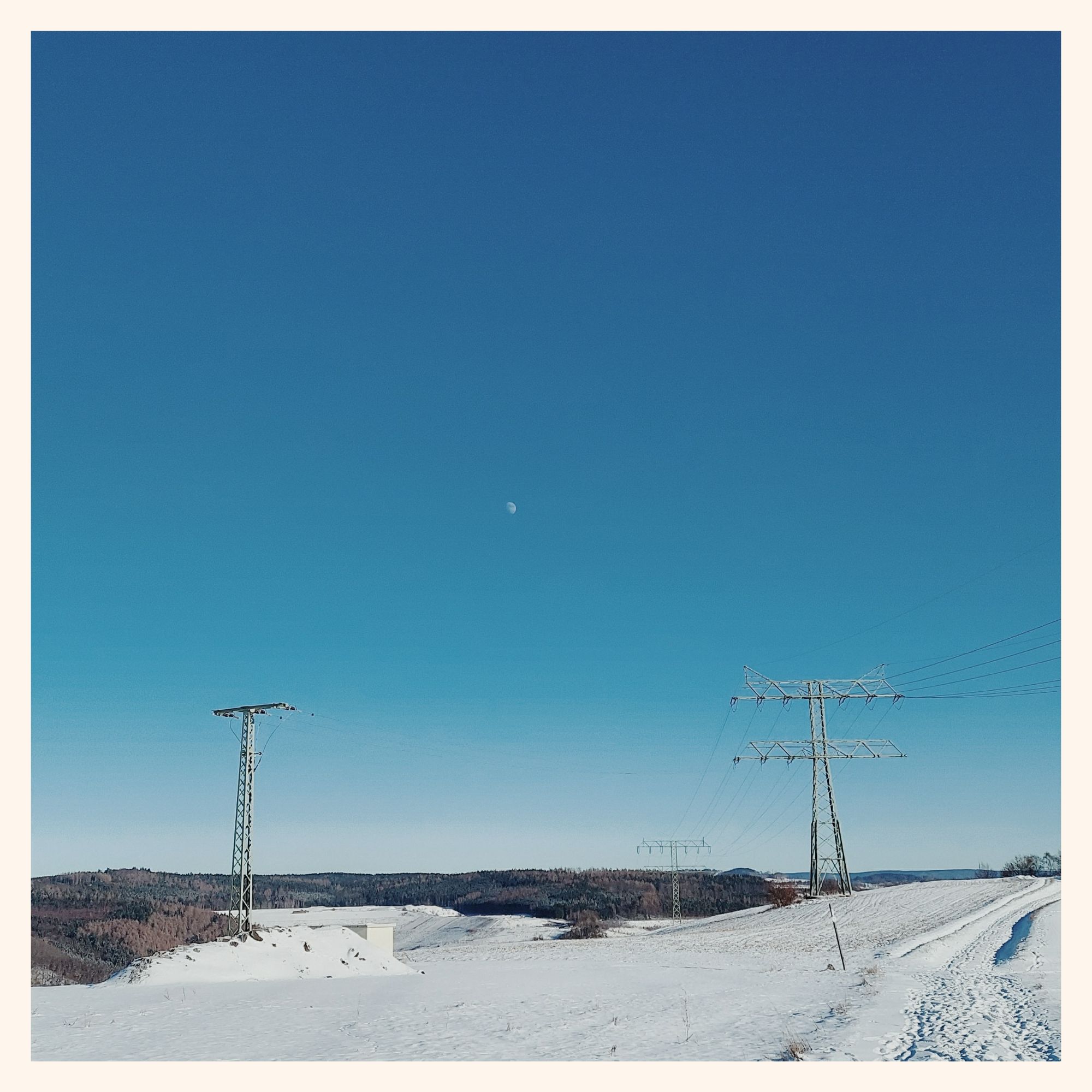 Pale blue sky over snow-covered meadows. A high-voltage road with a green pylon. Moon.