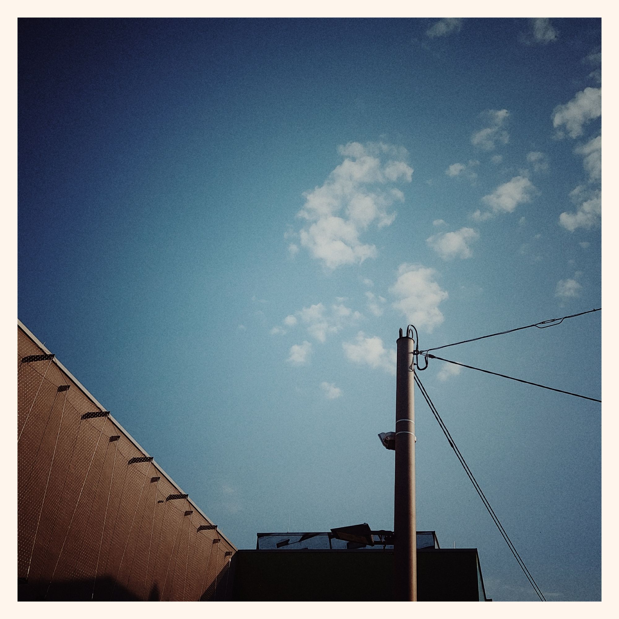 A quiet blue evening sky, some thin white clouds above an electric pylon and a concrete roof.