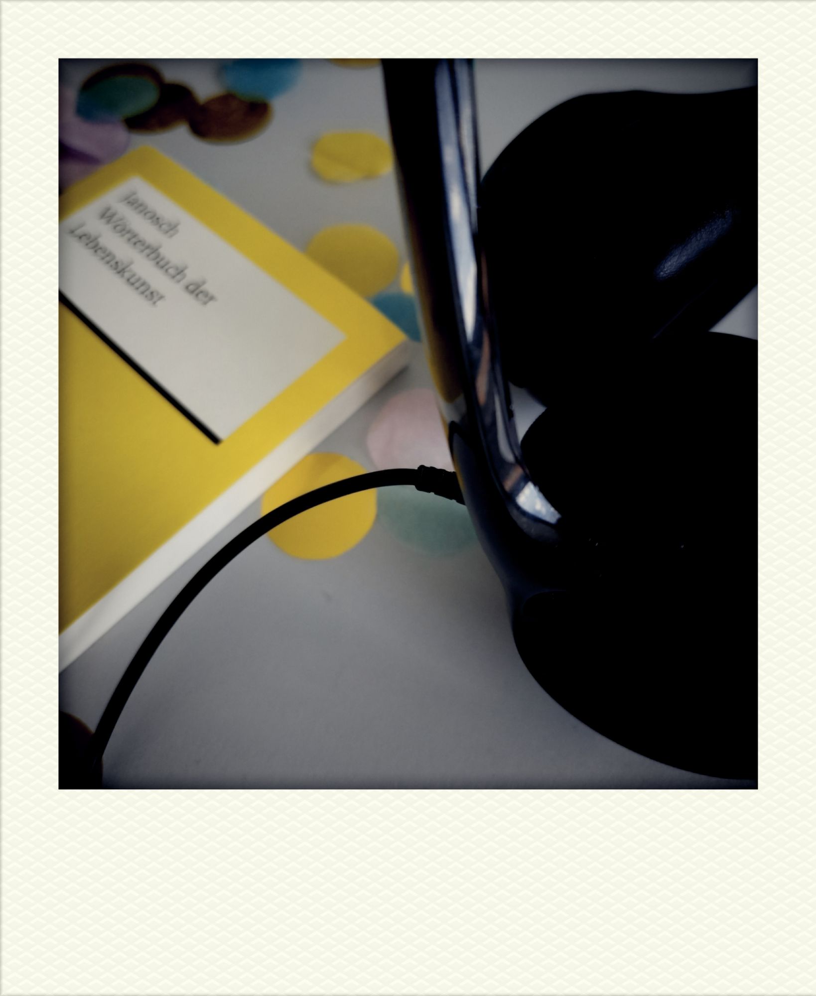 Schreibtischfoto: Headset. Bunte Schnipsel. Reclam-Heftchen Janosch, Wörterbuch der Lebenskunst.