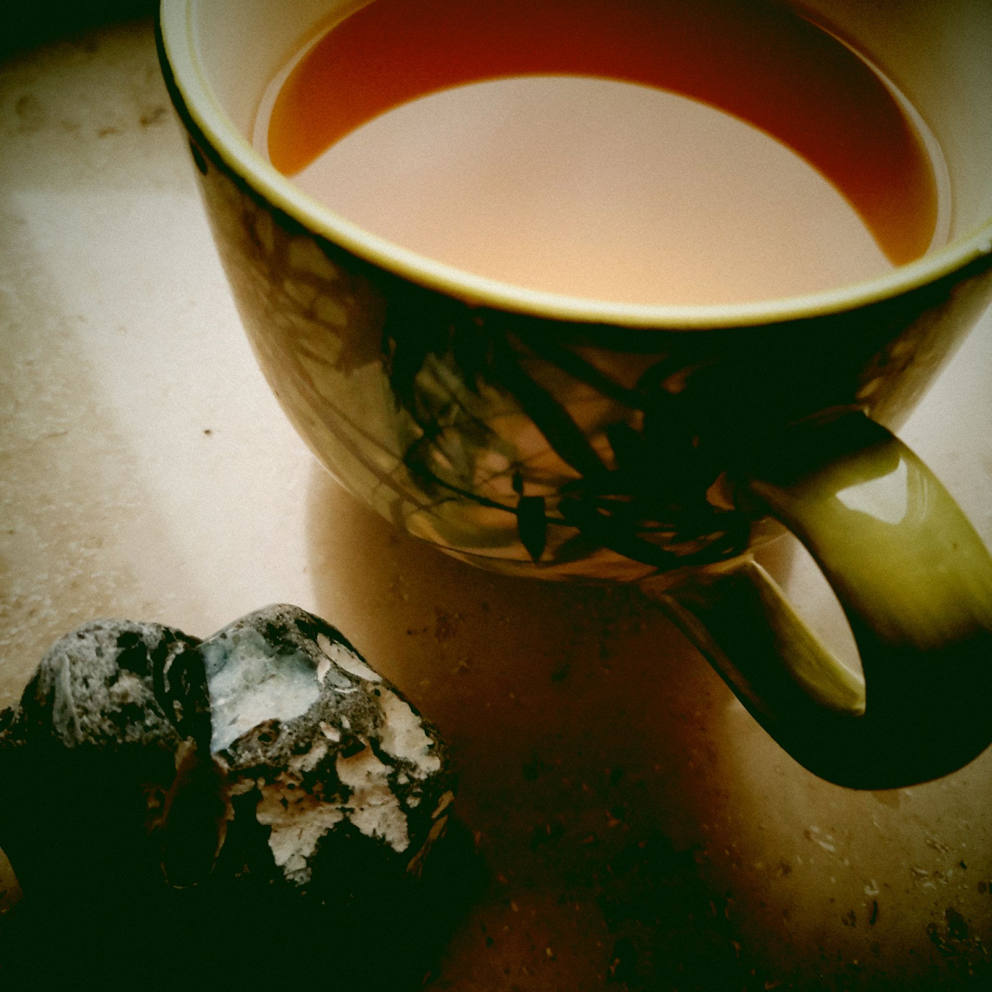 A huge green, leaf-decorated mug containing green tea. And an island stone, white, black. Both on a windowsill, reasonably close-up. Reflection of white sky on the liquid surface of the mug.