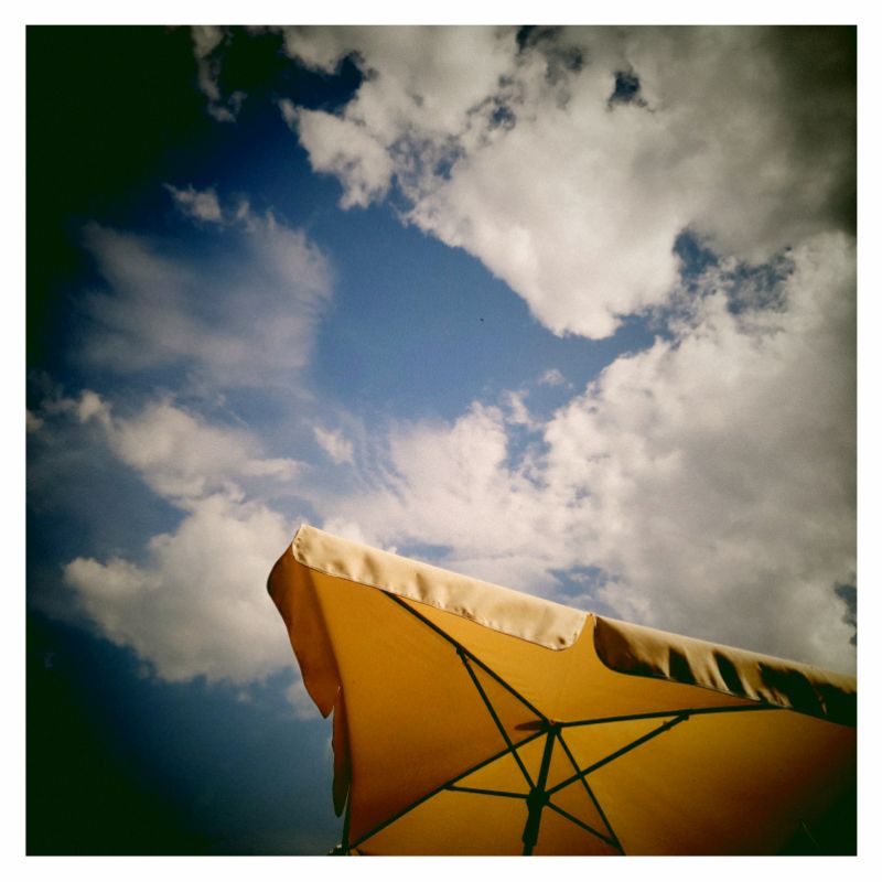 A squared umbrella flying in front of a blue and cloudy sky.