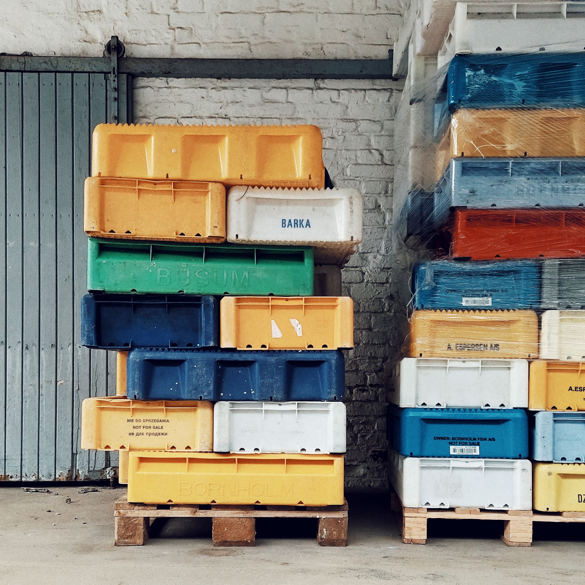 Fish shipping boxes in different colours, stacked in front of a white wall.