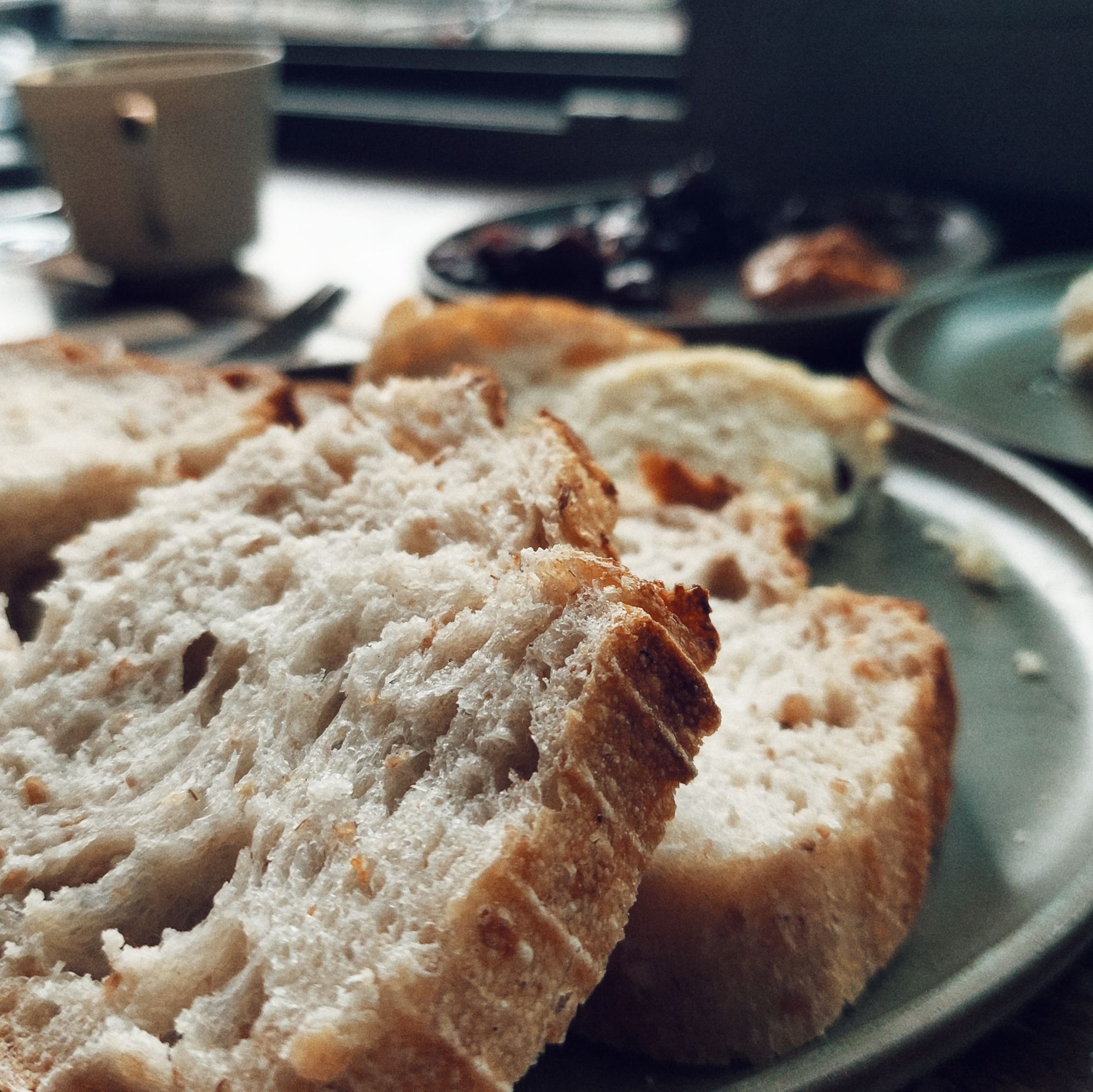 Brot auf einem grünen Teller. Kaffeetasse und Fenster im Hintergrund. 