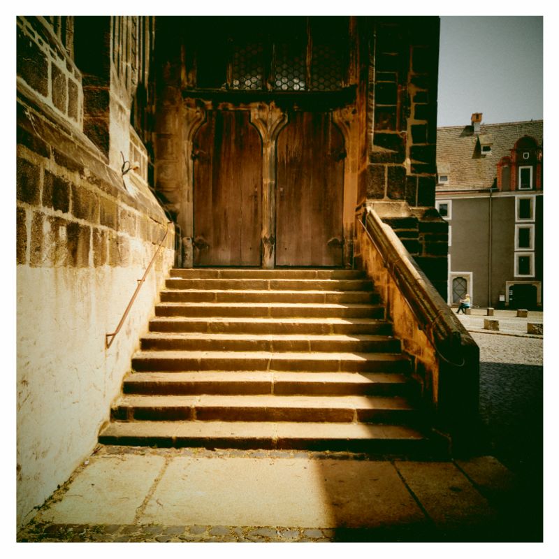 Staircase leading up to a closed church portal, in bright sun.