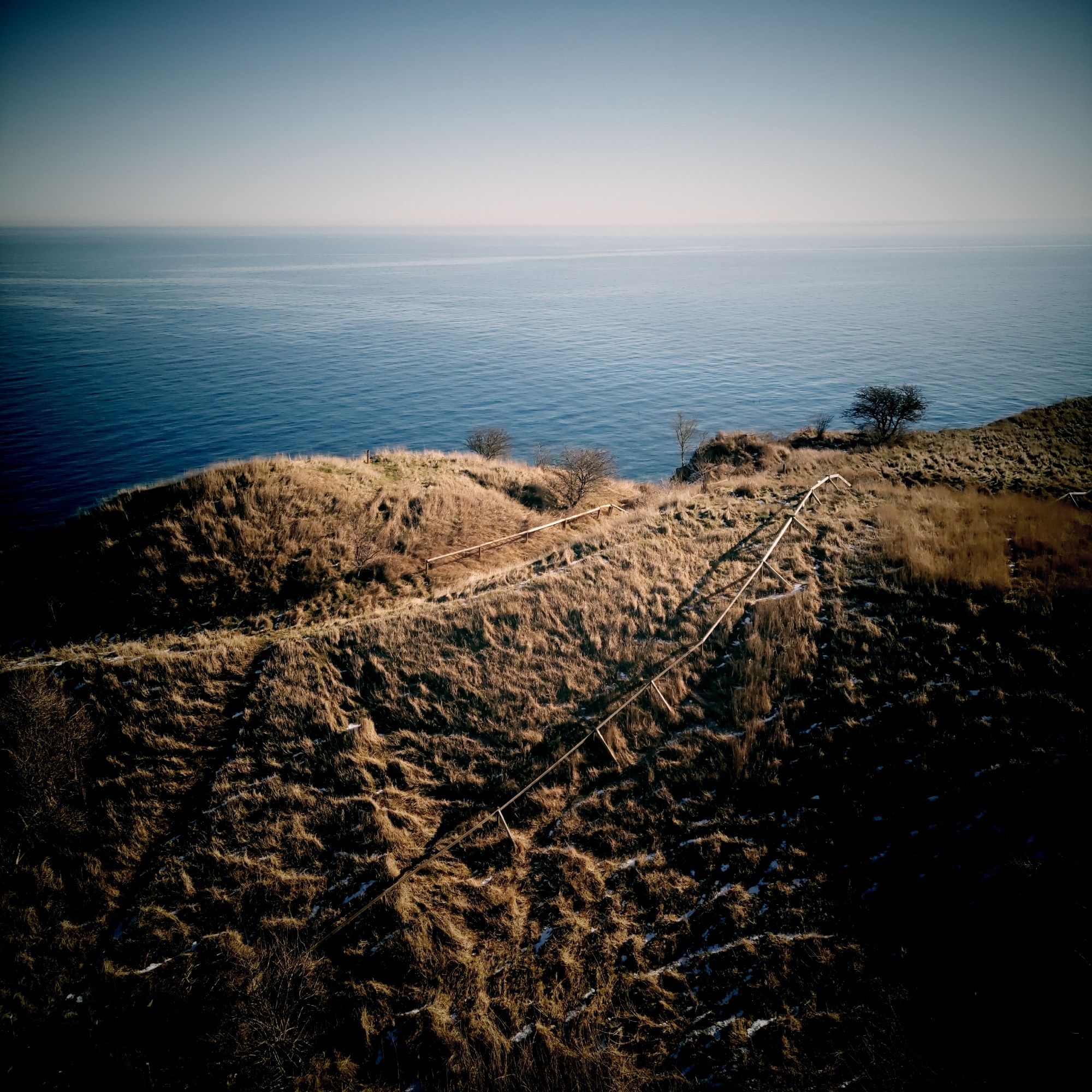 Brown bushy hills, a path and the sea behind. 