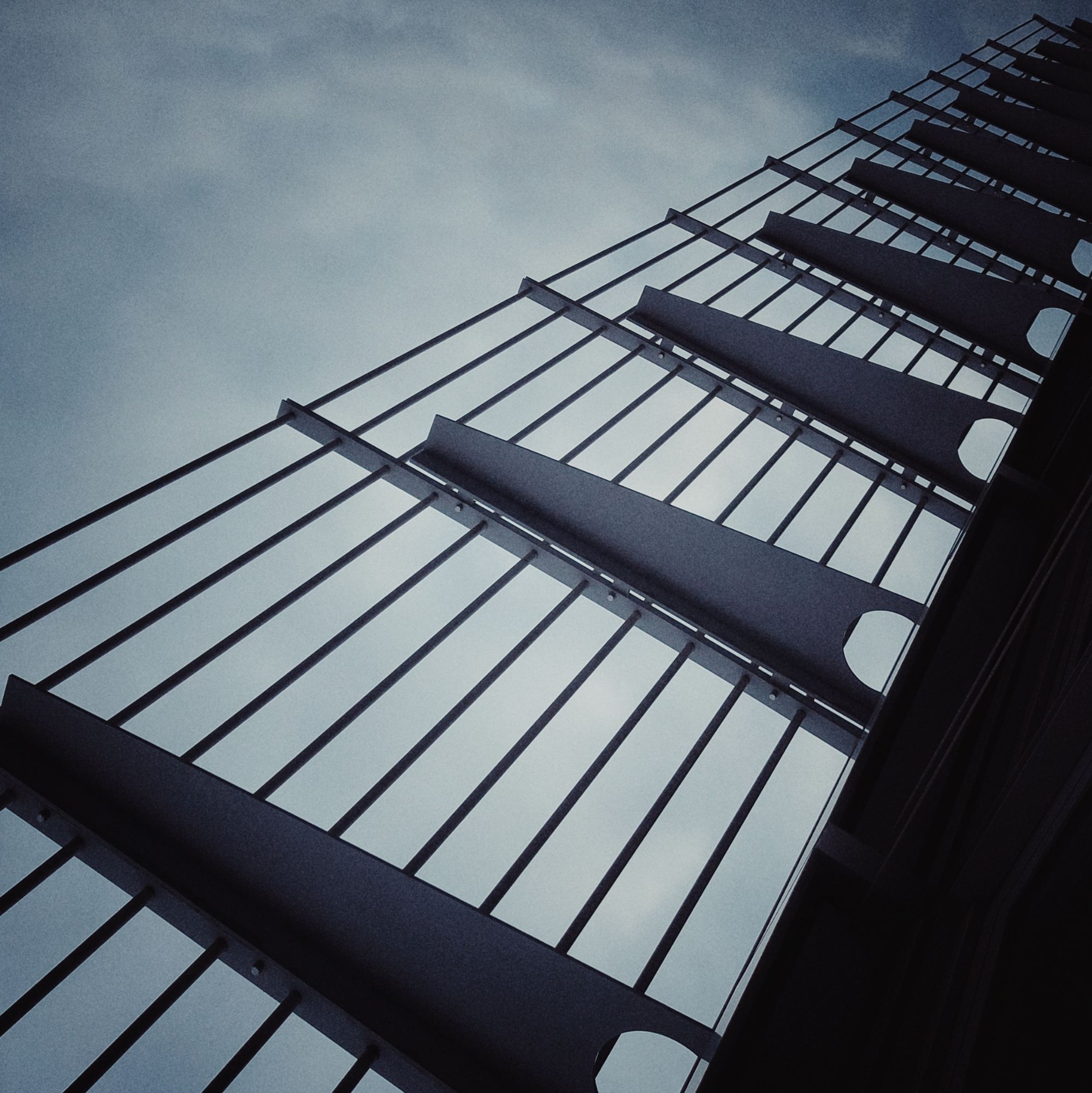 Umrandung eines Bürodachs. Stahlkonstruktion aus dünnen Streben, getragen von Blechen. Dahinter wolkiggrauer Himmel.