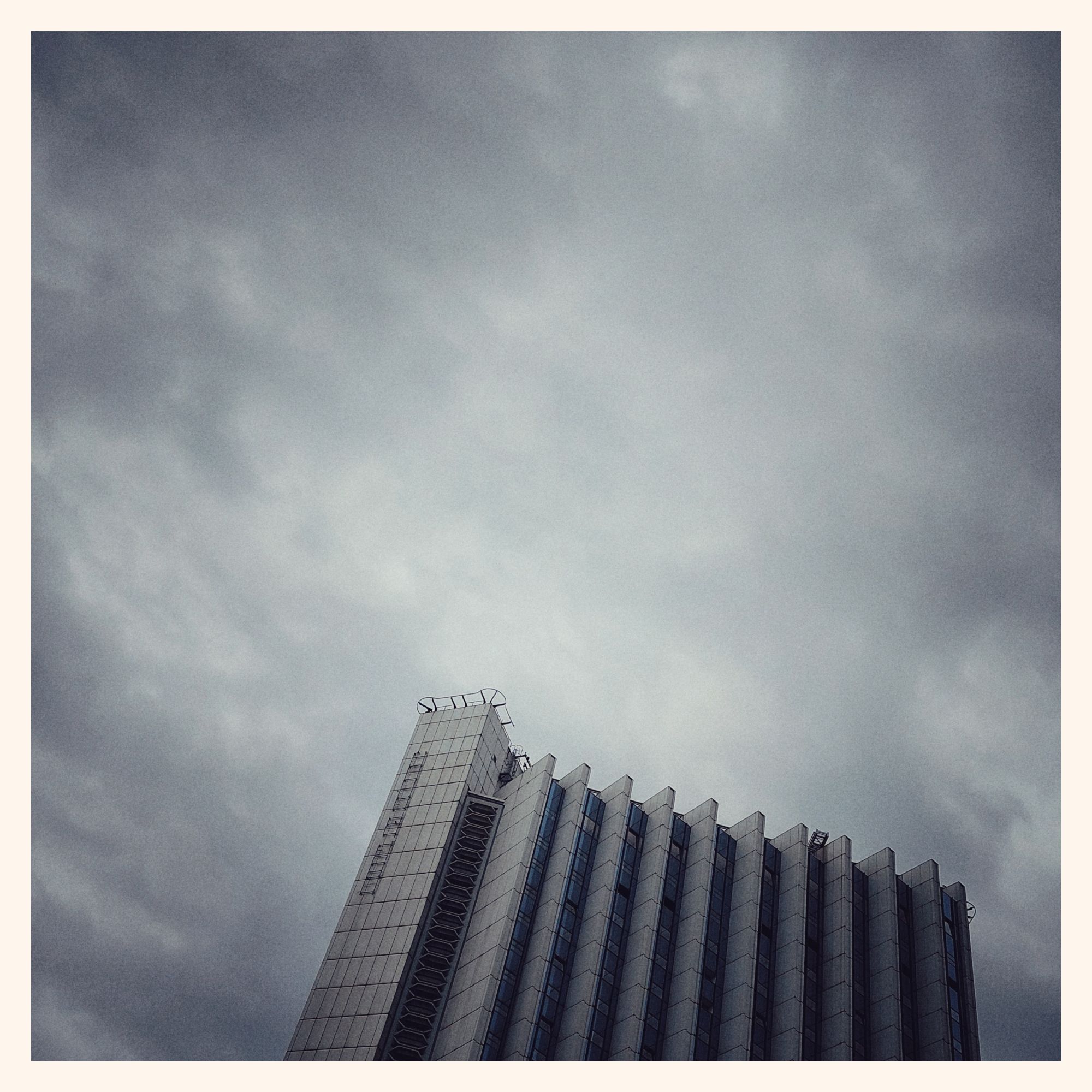 A highrise in front of a white and grey sky.