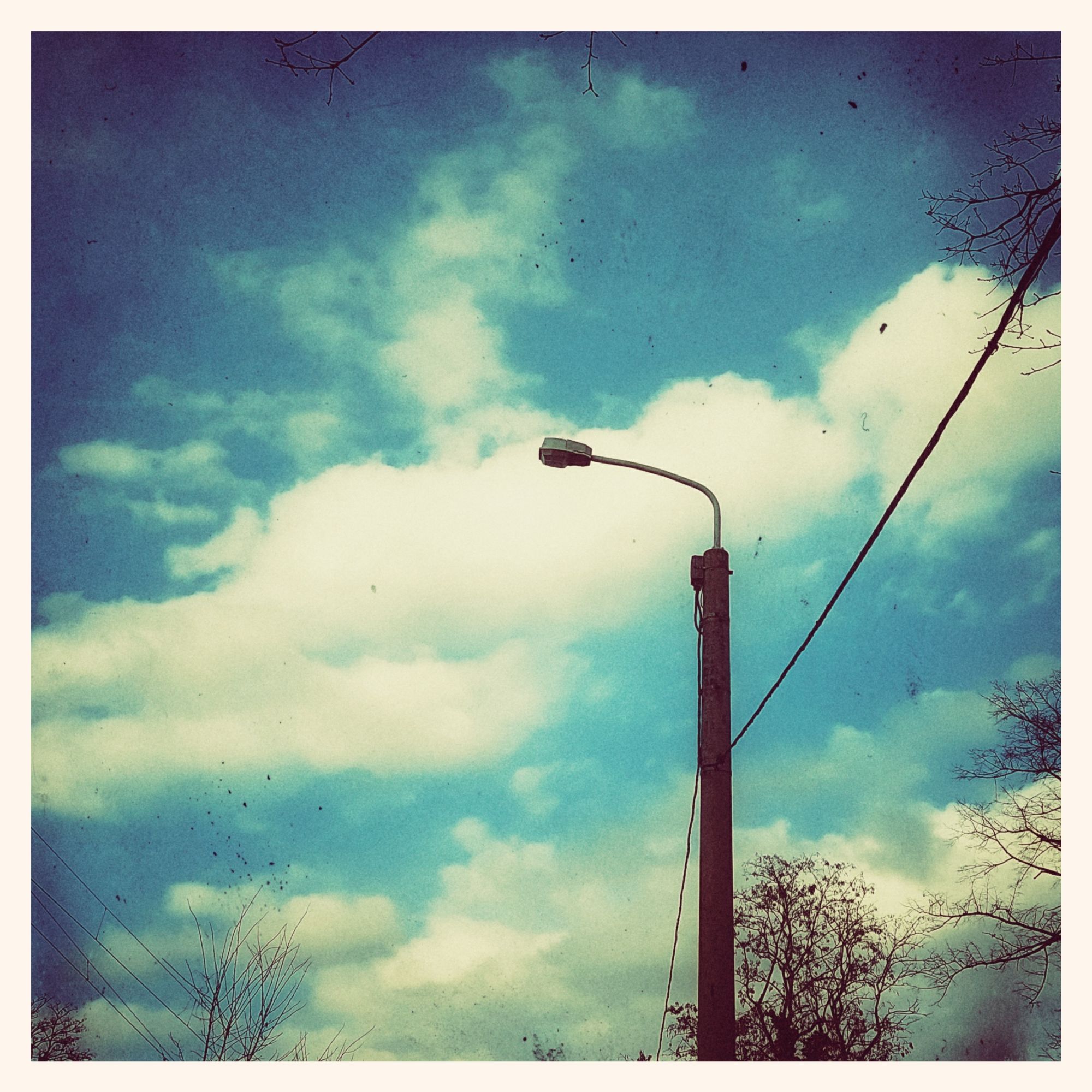 Streetlight and white clouds in front of a mostly blue sky. Vintage photo style.