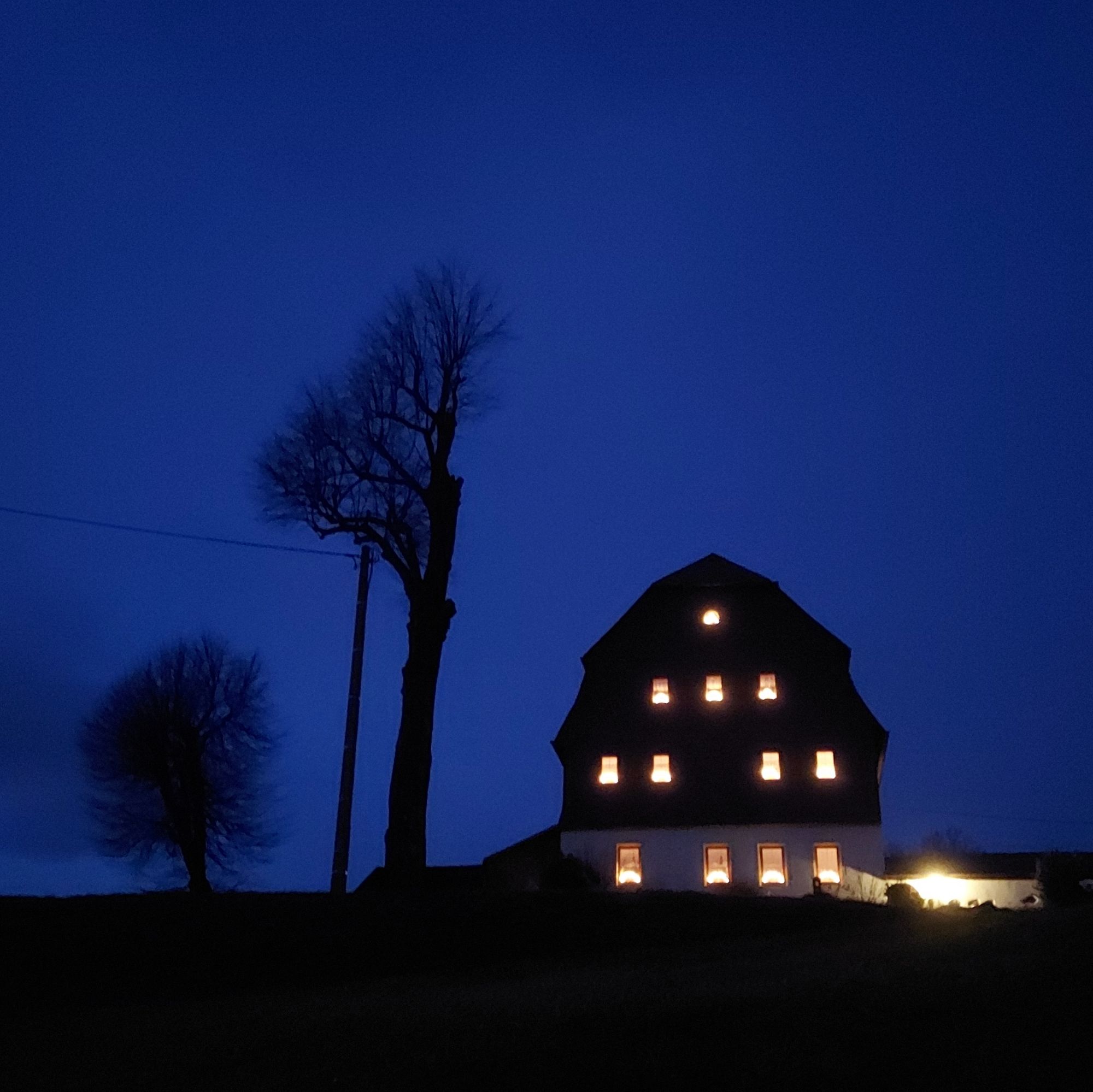 A brightly illuminated farmer house in late dusk.