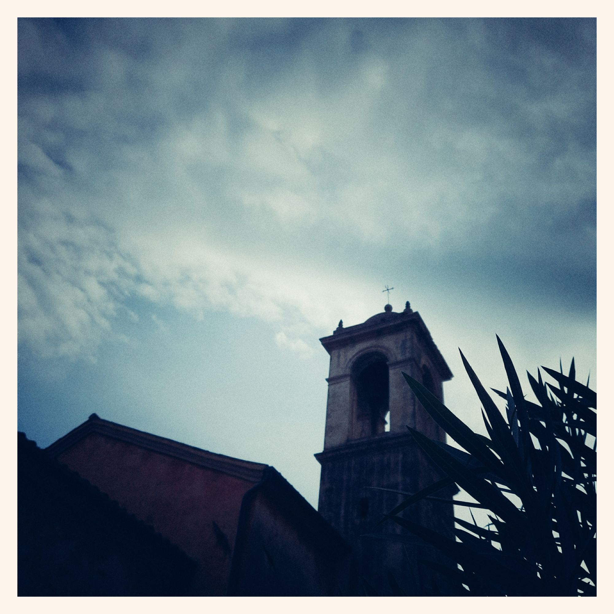 An old belfry and church roof in front of a bright sunset sky. Oleander leaves in front.