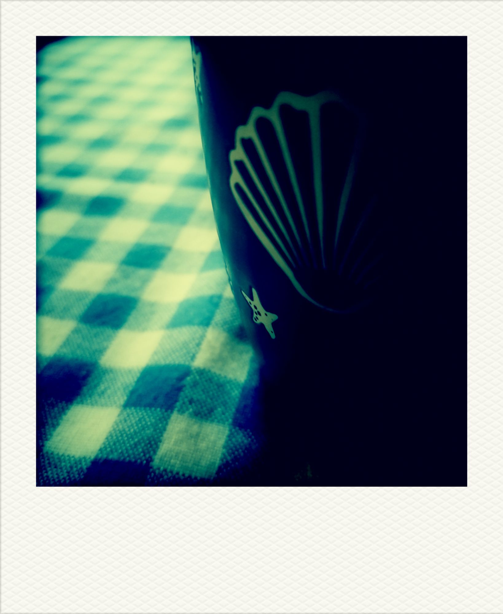 Kaffeetasse mit Stern und Muschel auf karierter Tischdecke.