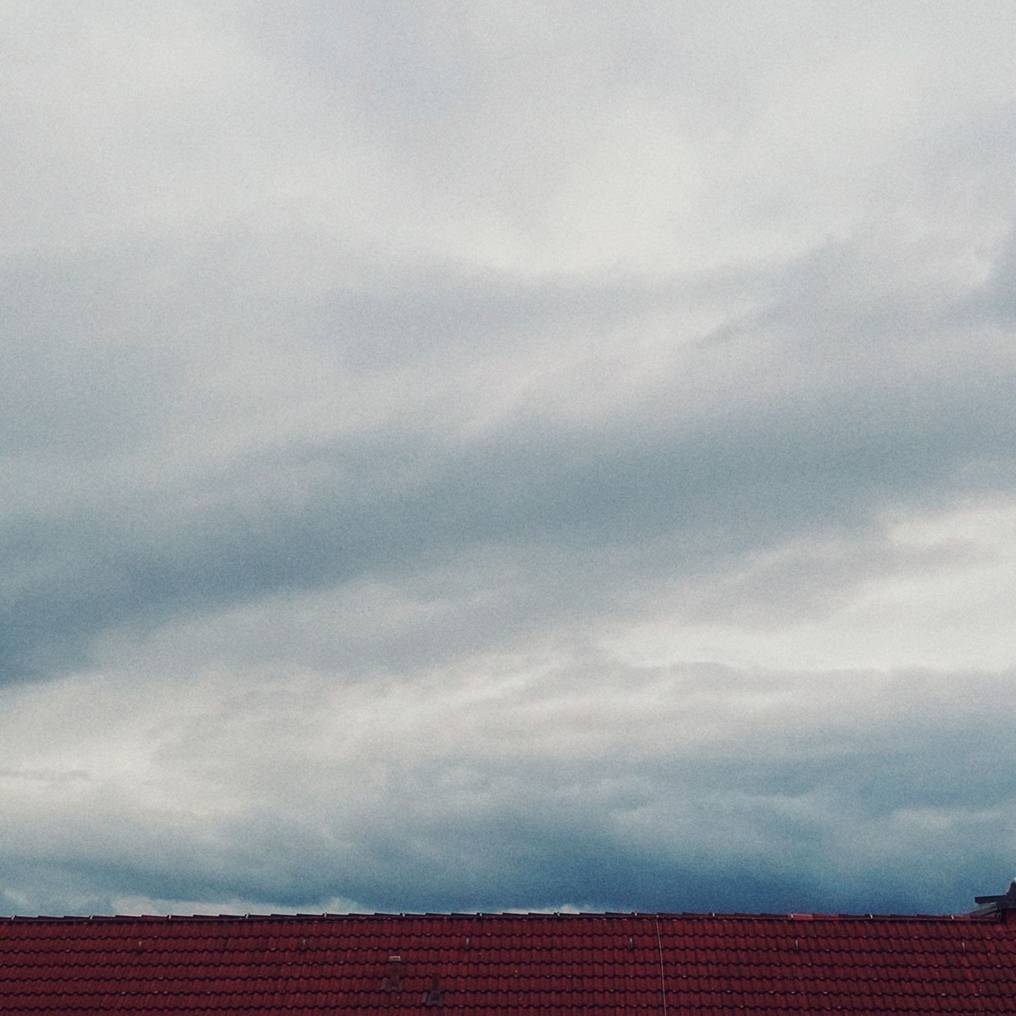 Strong grey clouds above a reddish shingle roof.