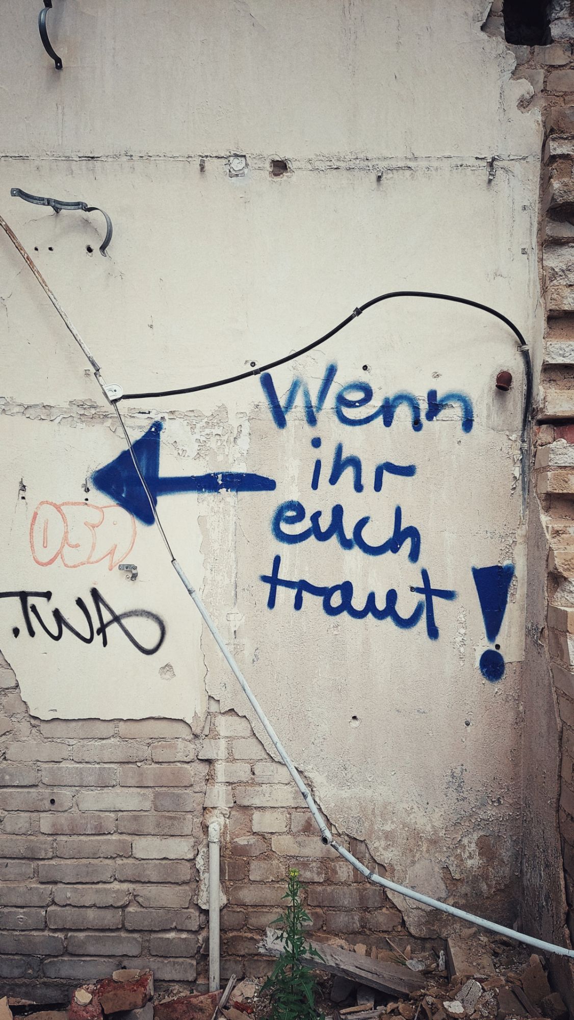 Wall of an abandoned building. An arrow pointing inwards, a text reading IF YOU DARE in German.