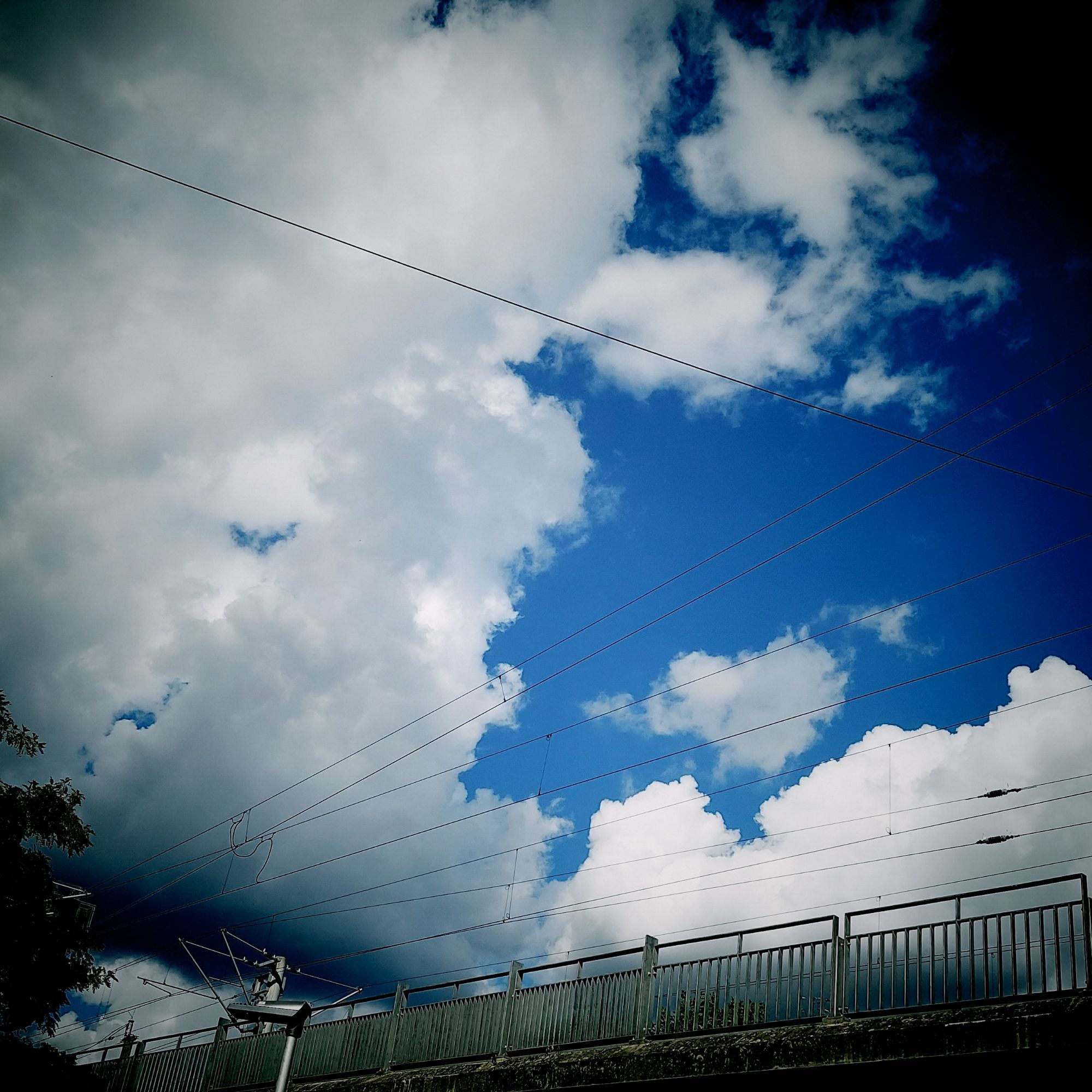 Wolken, weiß und grau am Himmel über einem Bahndamm.