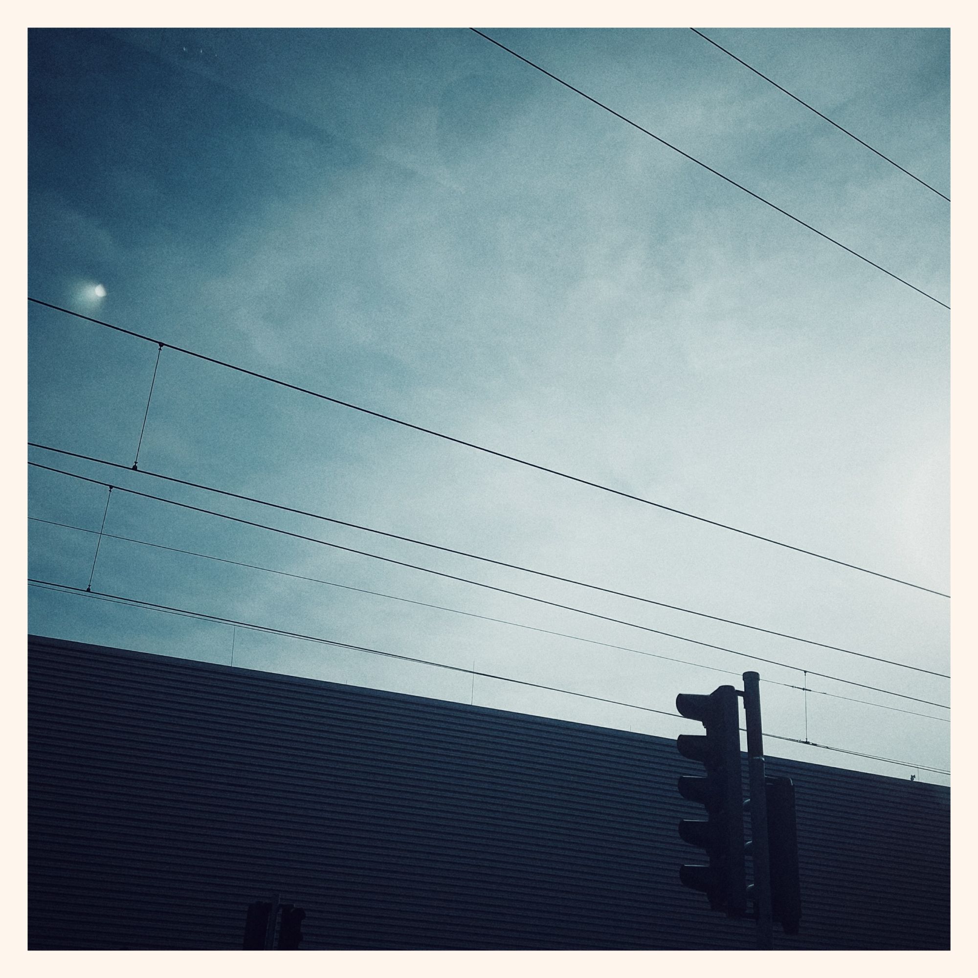 Bright pre-sunset sky above a concrete building. Traffic lights, power lines, and a brief lens flare.