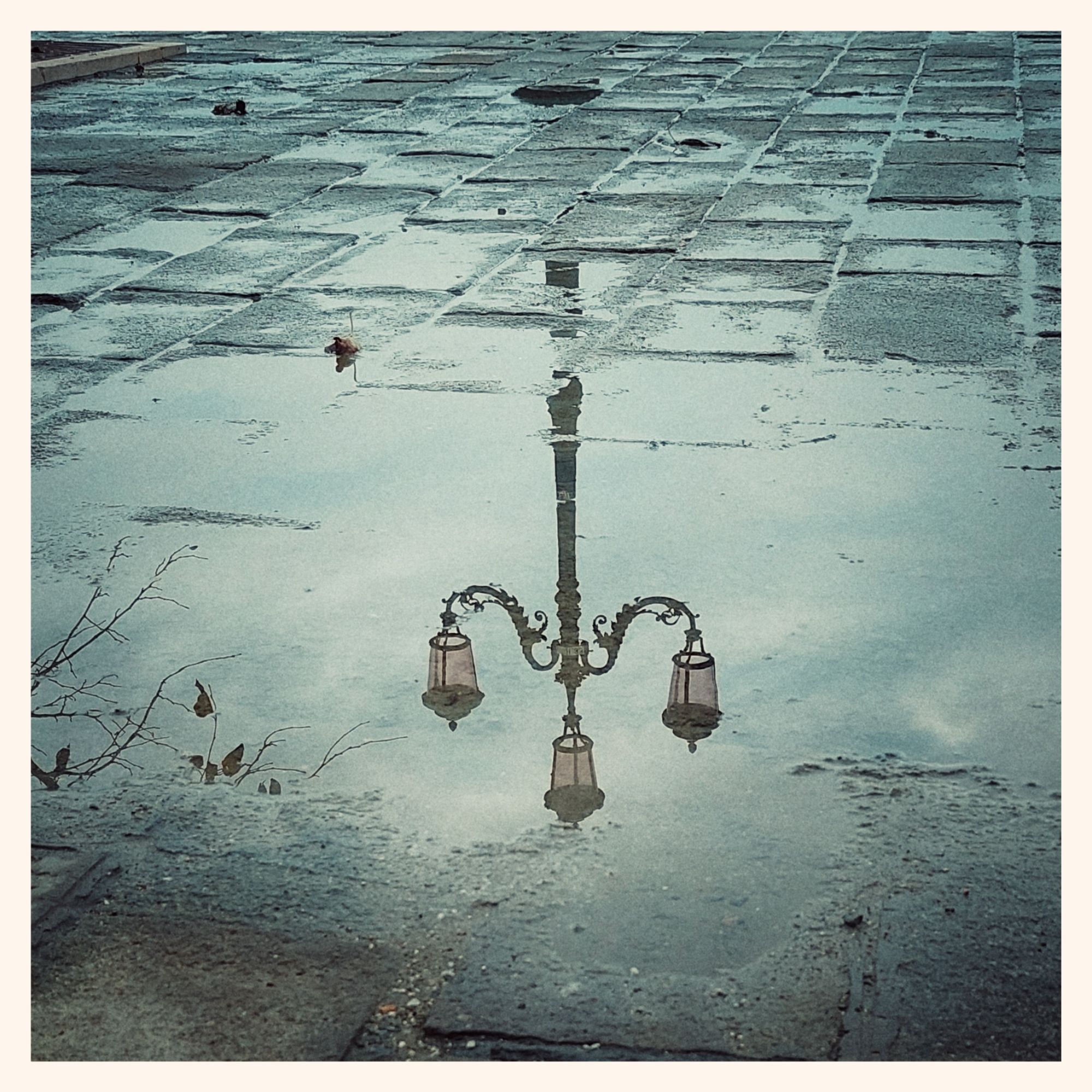 Reflection of grey sky and a lantern in a puddle on a way made of stones.