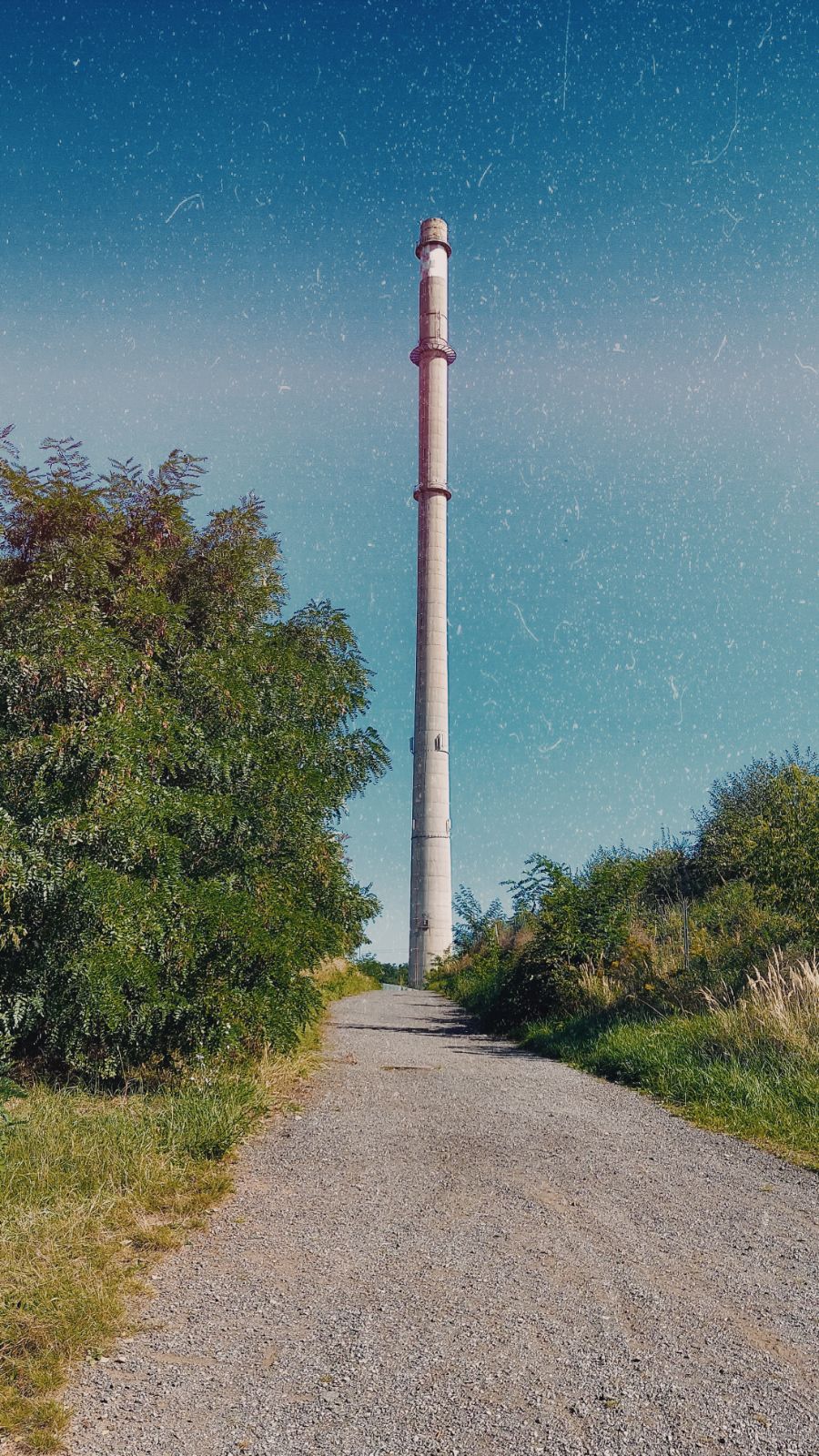 Chimney of some industrial facility behind the green, at the end of a way paved with small stones.