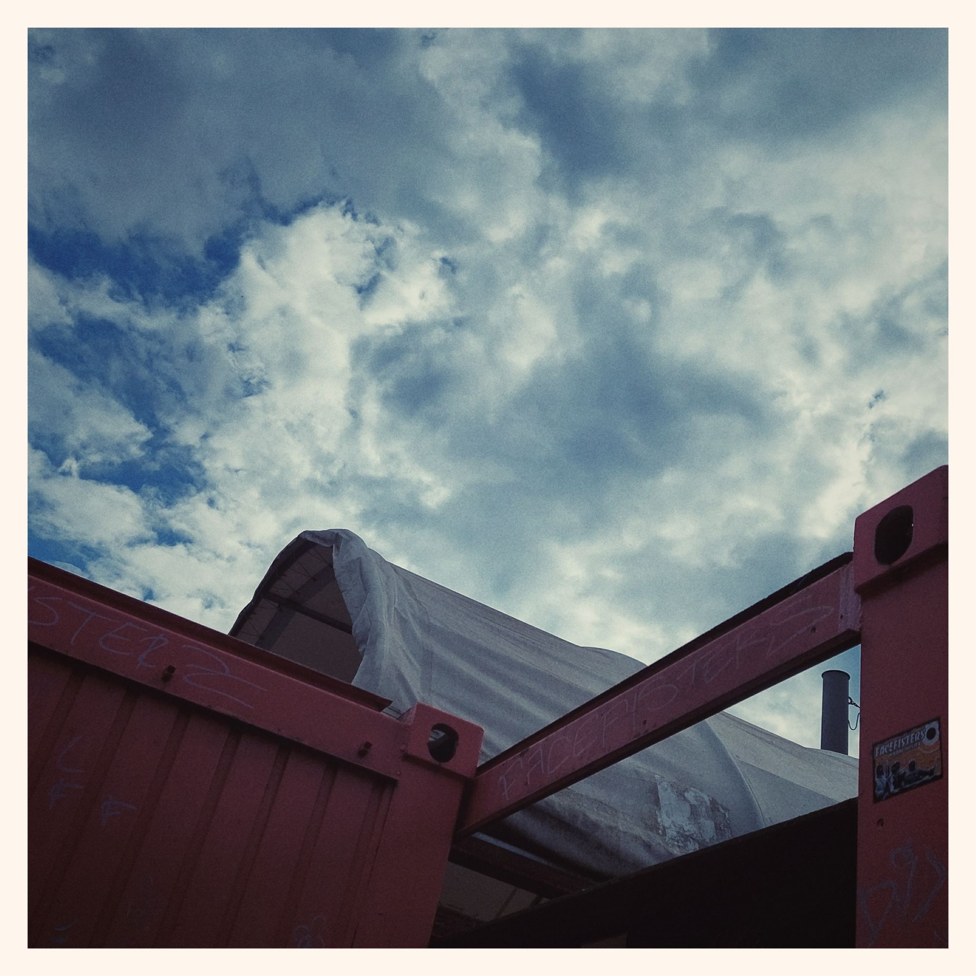 Troubled sky above a roof of tent fabric and steel girders.