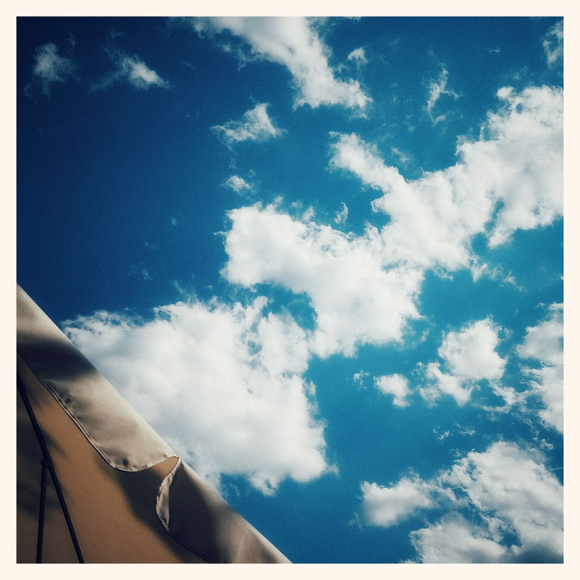 High contrast sky, white clouds on a deep blue backdrop. Part of an umbrella on the lower left.