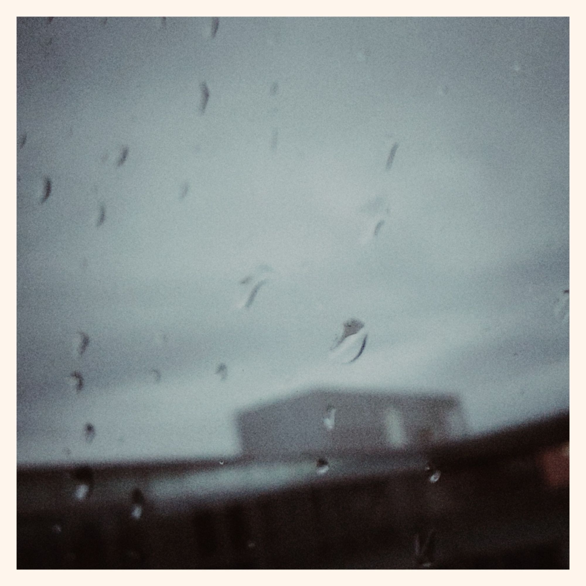 Grey sky, concrete facade and raindrops on a windowpane in front.