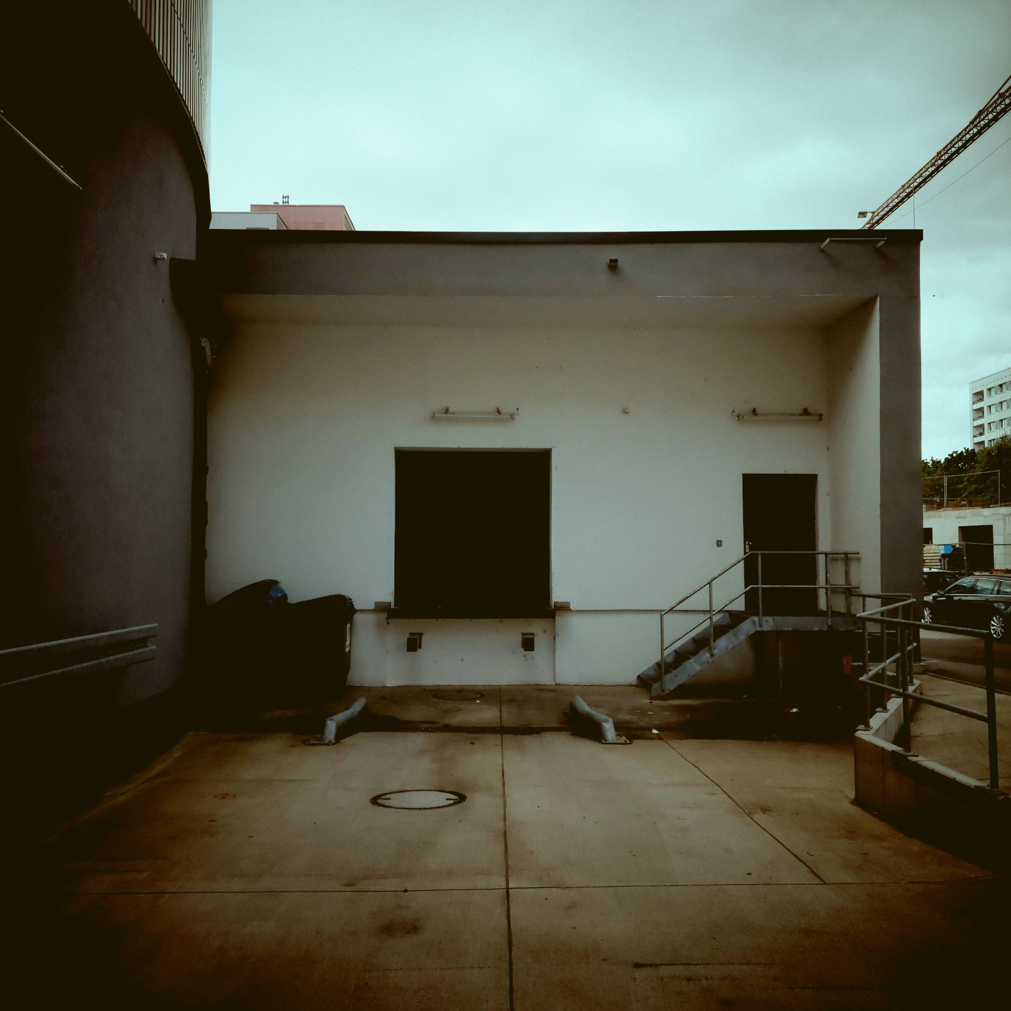 A concrete building, high-rise behind, empty space in front.