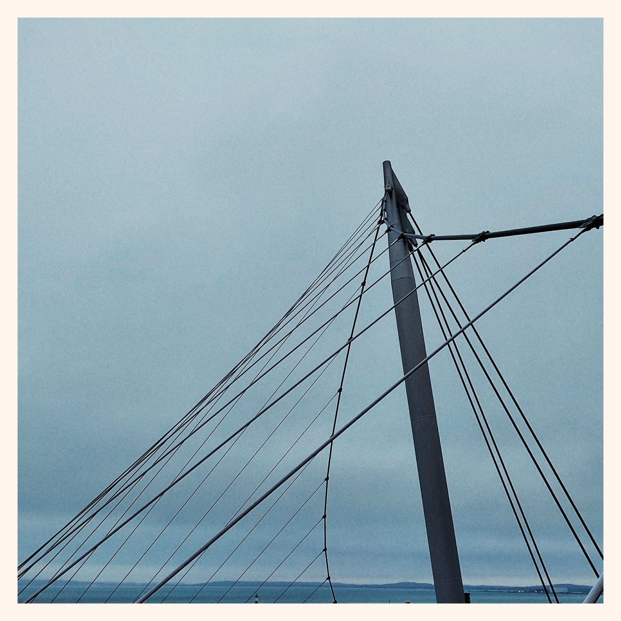 A modern steel rope bridge in front of a light grey sky.