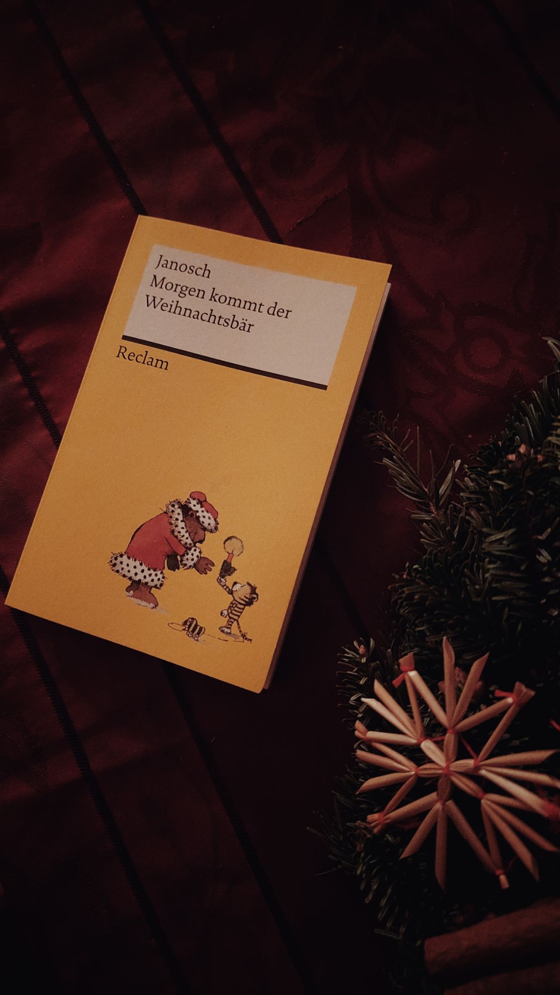 A copy of a Janosch christmas book on a red tablecloth, next to a straw star