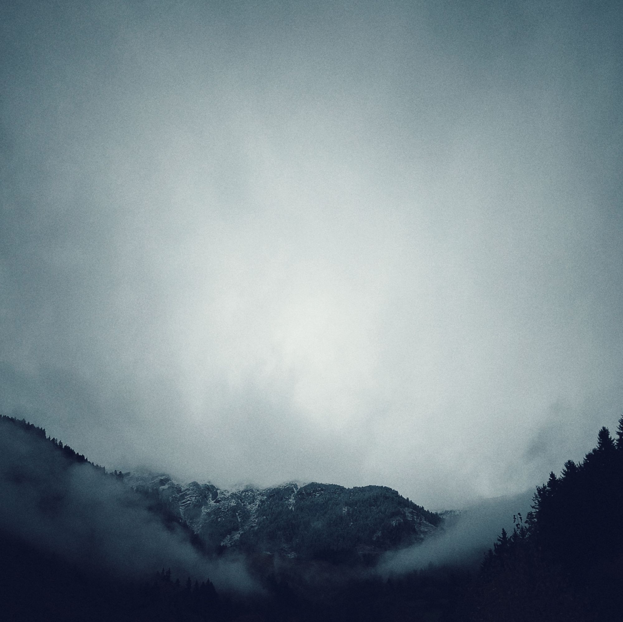 Bright clouds above mountains and trees. Some snow on the rocks.
