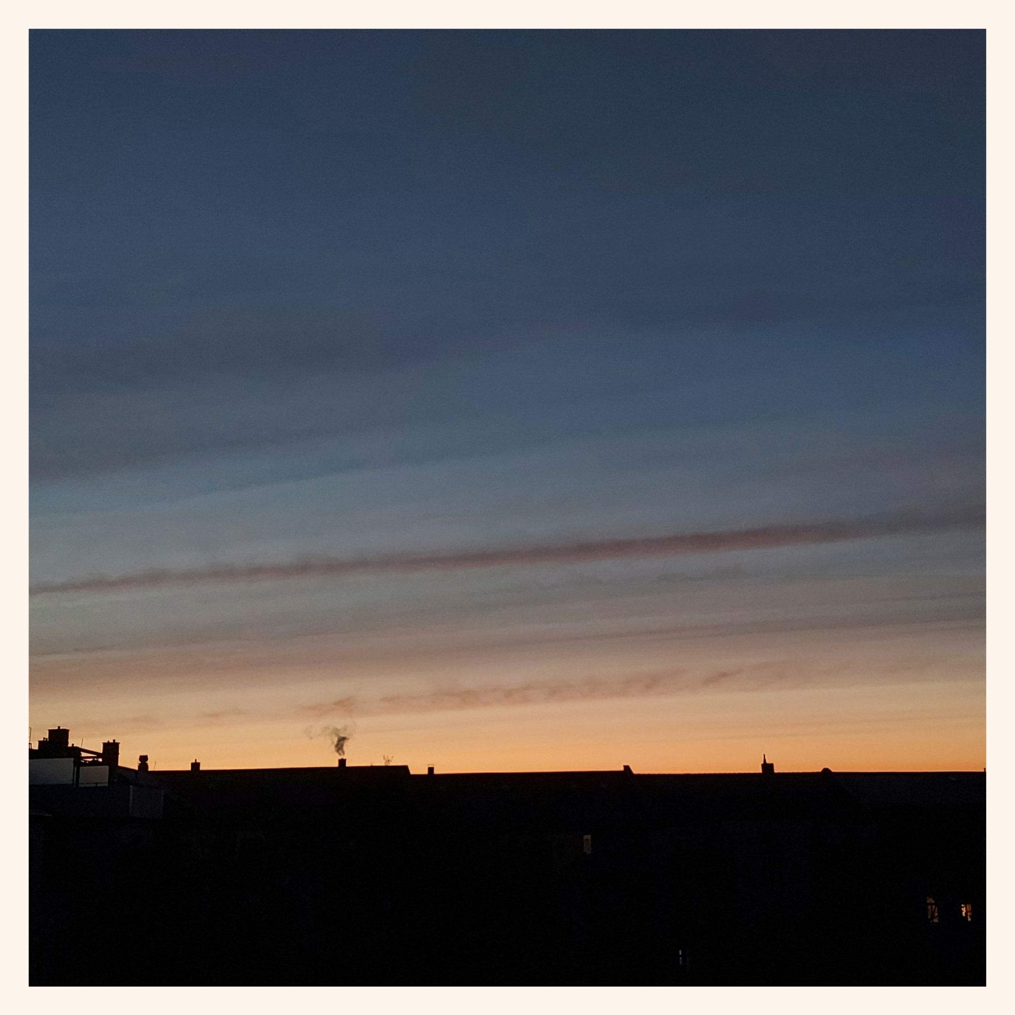 Early morning sky, before sunrise. Quiet colours, thin lines of clouds. Houses and chimneys below.