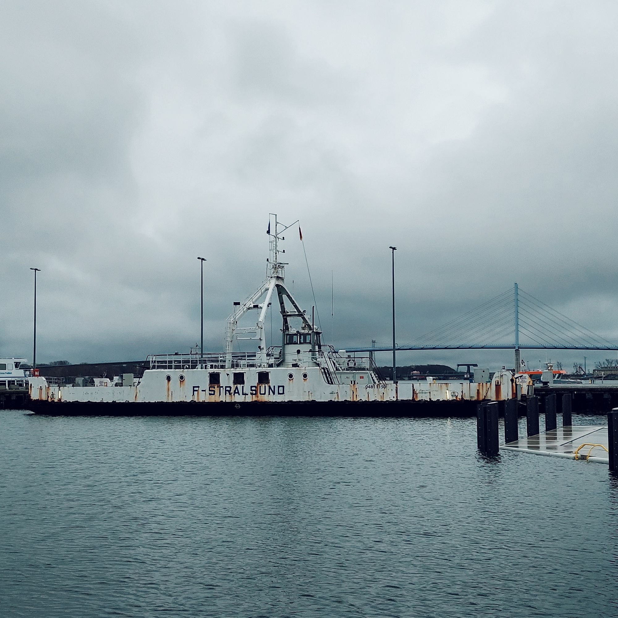 A ship in Stralsund mole, surrounded by grey water. Ruegen bridge behind.