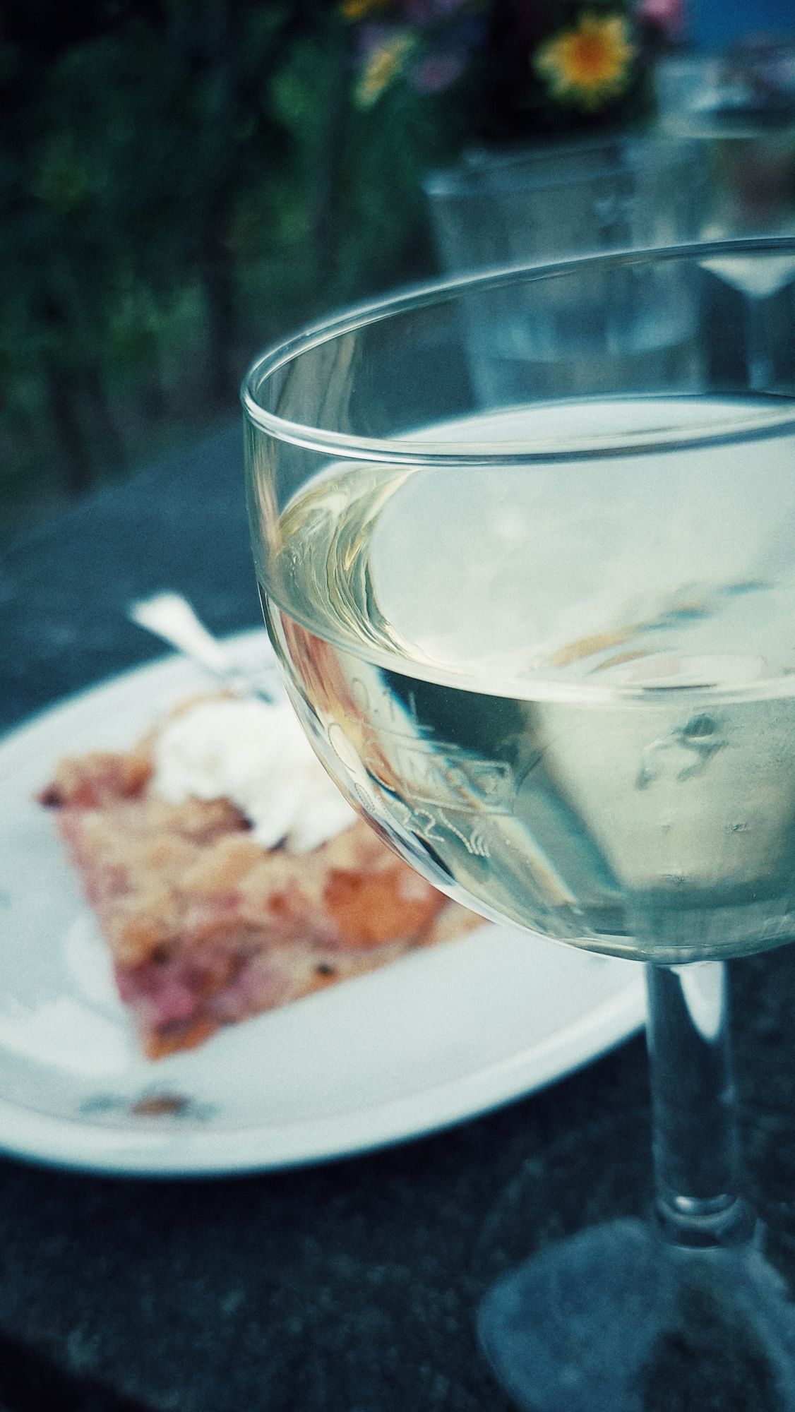 A glass of white wine, cake on a plate behind.