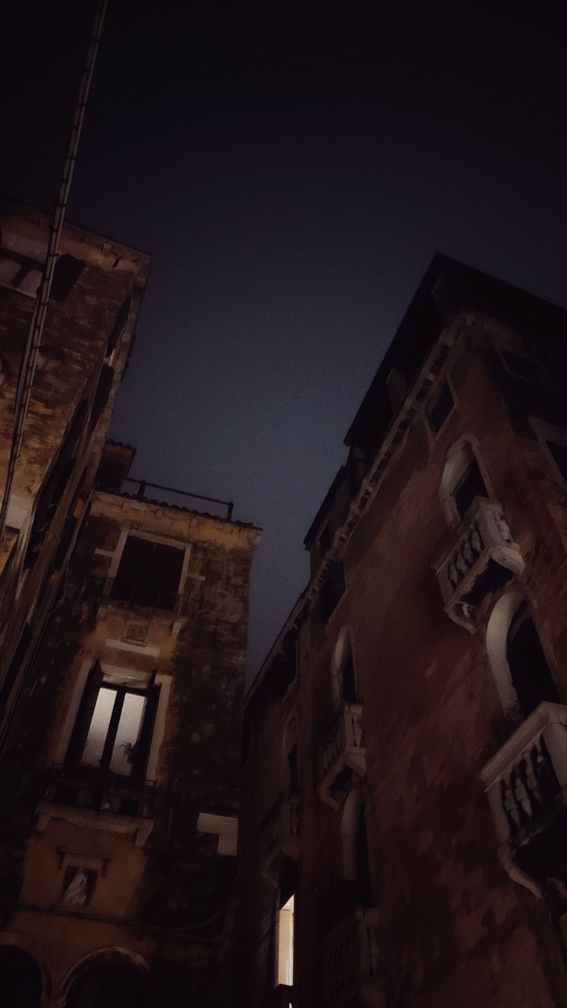 Old city houses in front of a dim nightsky. All windows but one are dark.