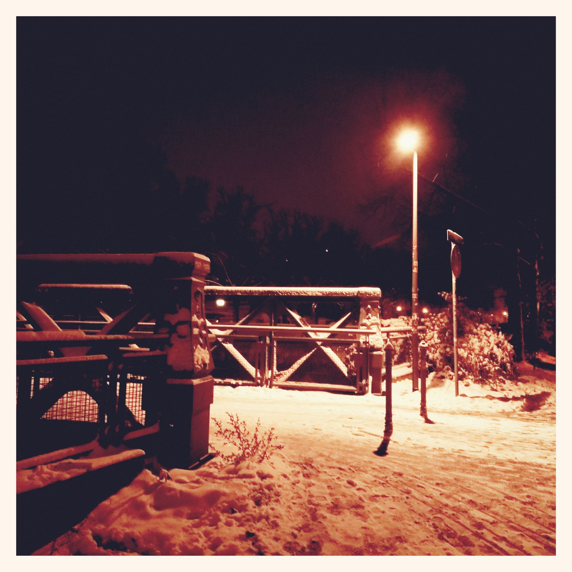 An iron bridge in snow, and a lantern shedding its light on it.