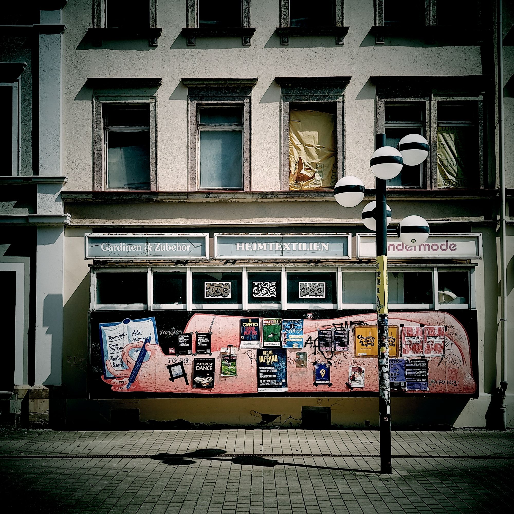An old facade of an abandoned house. Front of a former store, windows closed with wooden boards and decorated with ads for various local events in future and past.