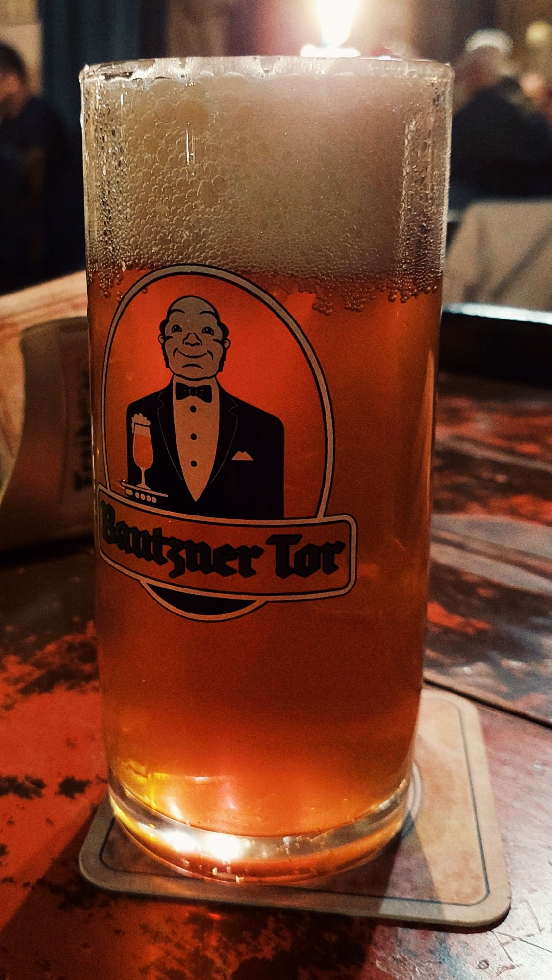 A glass of beer with a stylized waiter on it, and the name of the restaurant. 