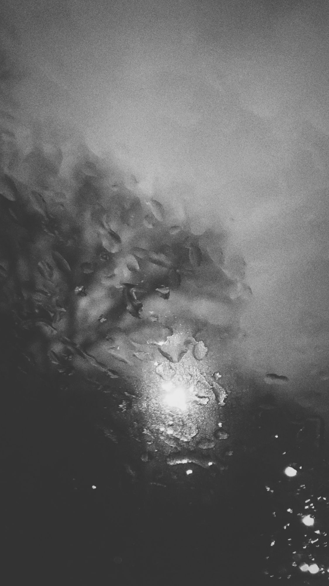 Trees and a streetlight behind a window. Raindrops in front.