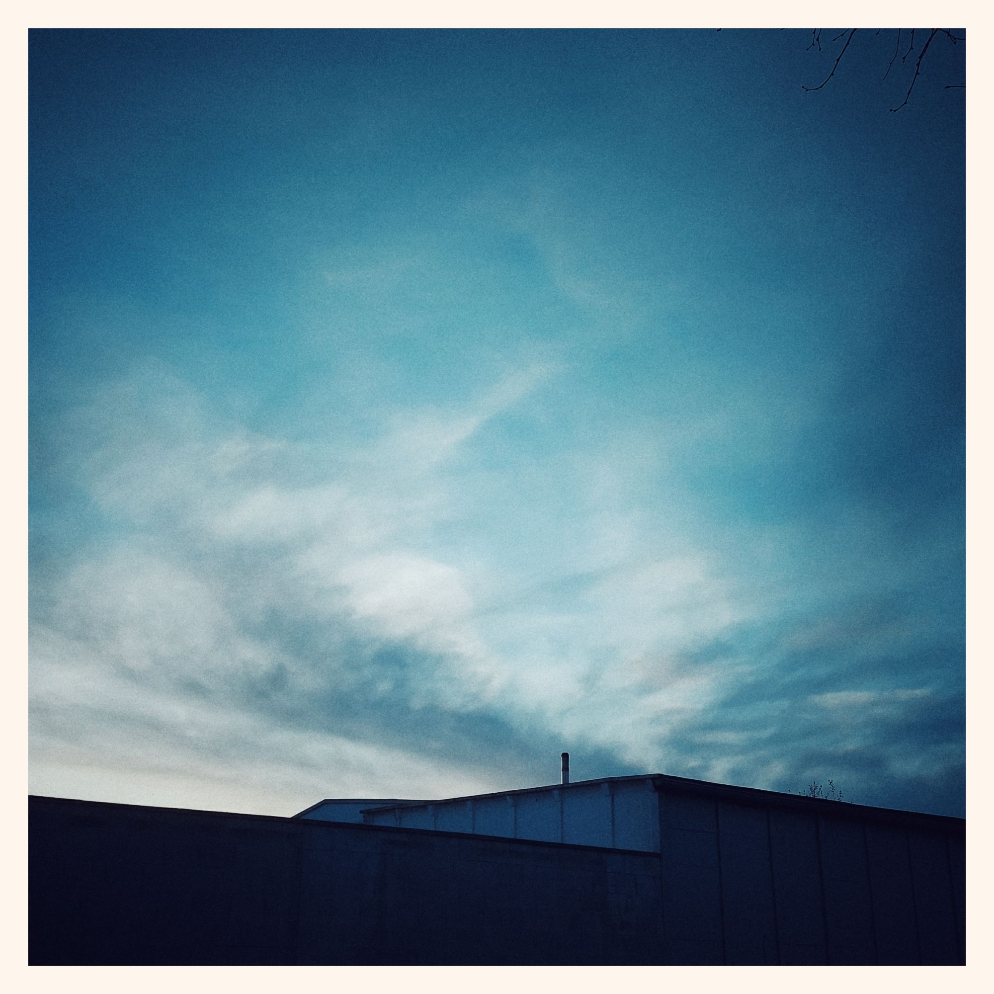 Early dusk sky, a slightly wing-shaped cloud and some last sunlight above flat roofs of industrial buildings.