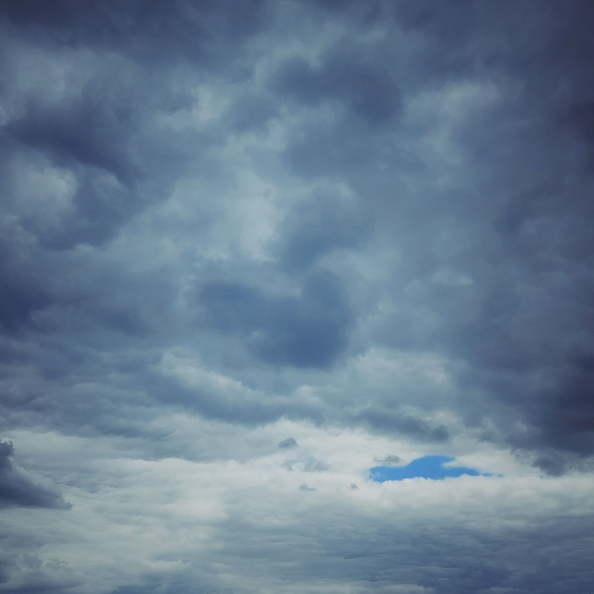 Turbulente Wolken mit einer kleinen Insel blauen Himmels.`