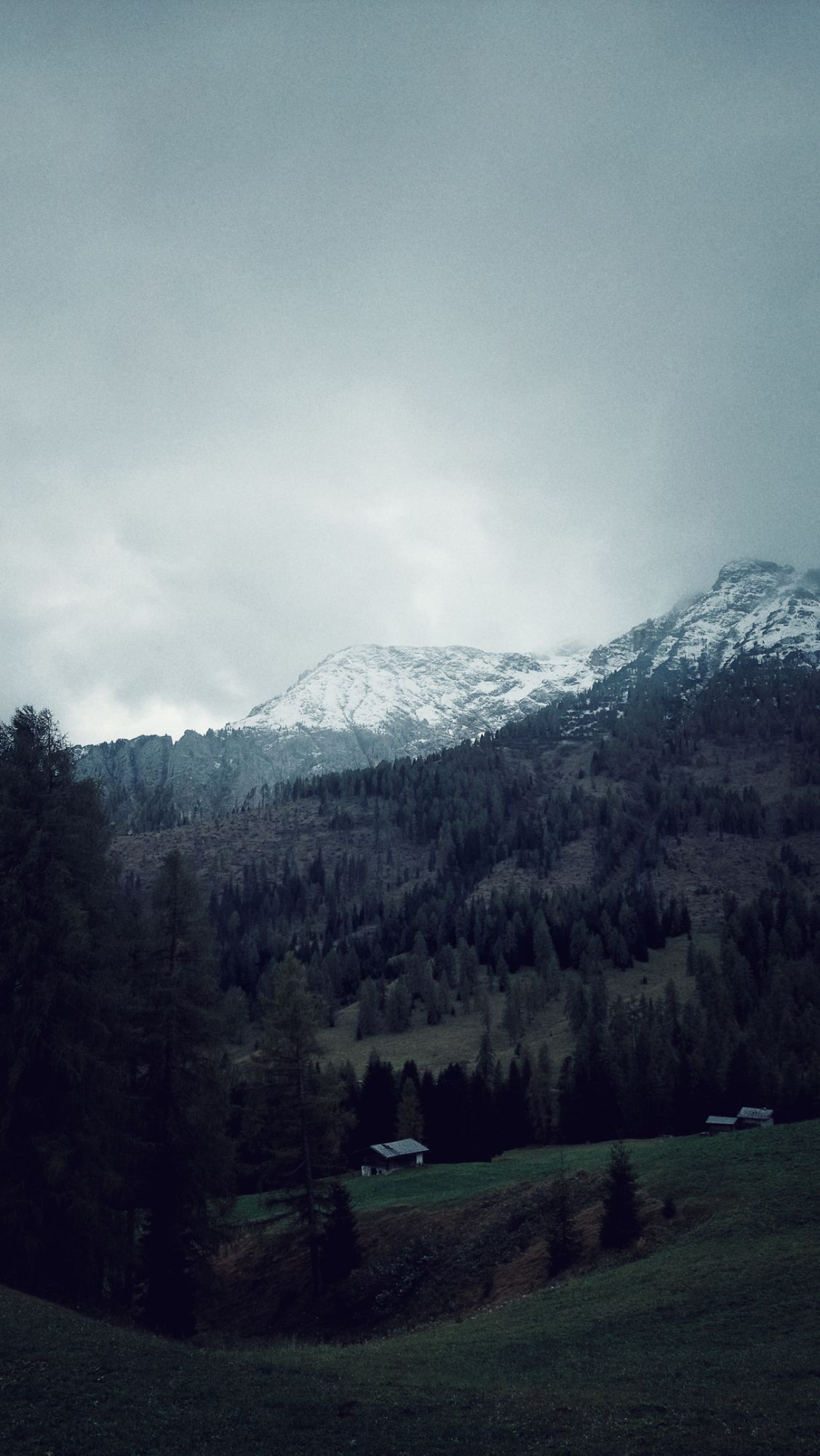 Snow covered mountains above green meadows. Clouds surrounding the rocks.