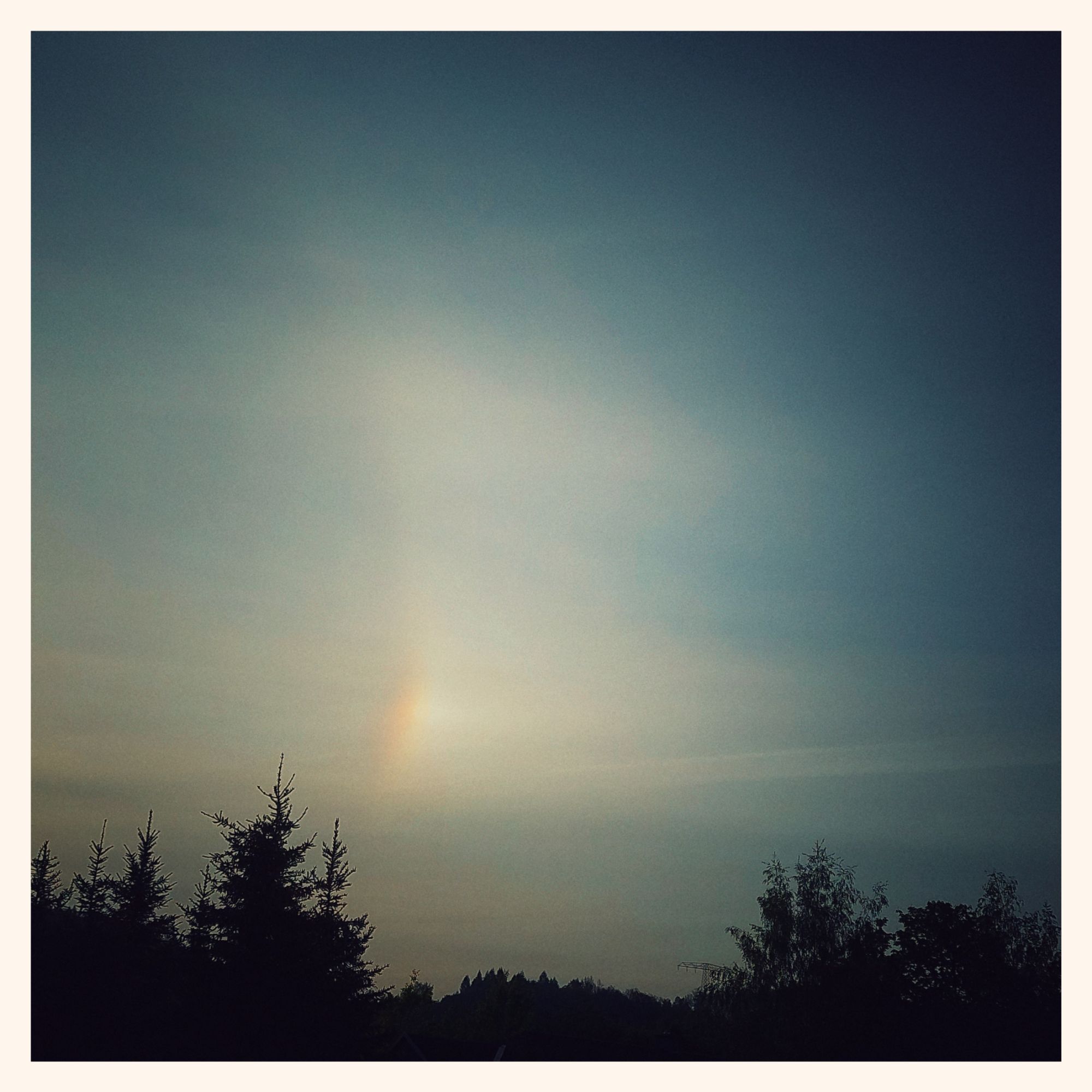 Morning sky above the forest. Sunrise and a rainbow flare.
