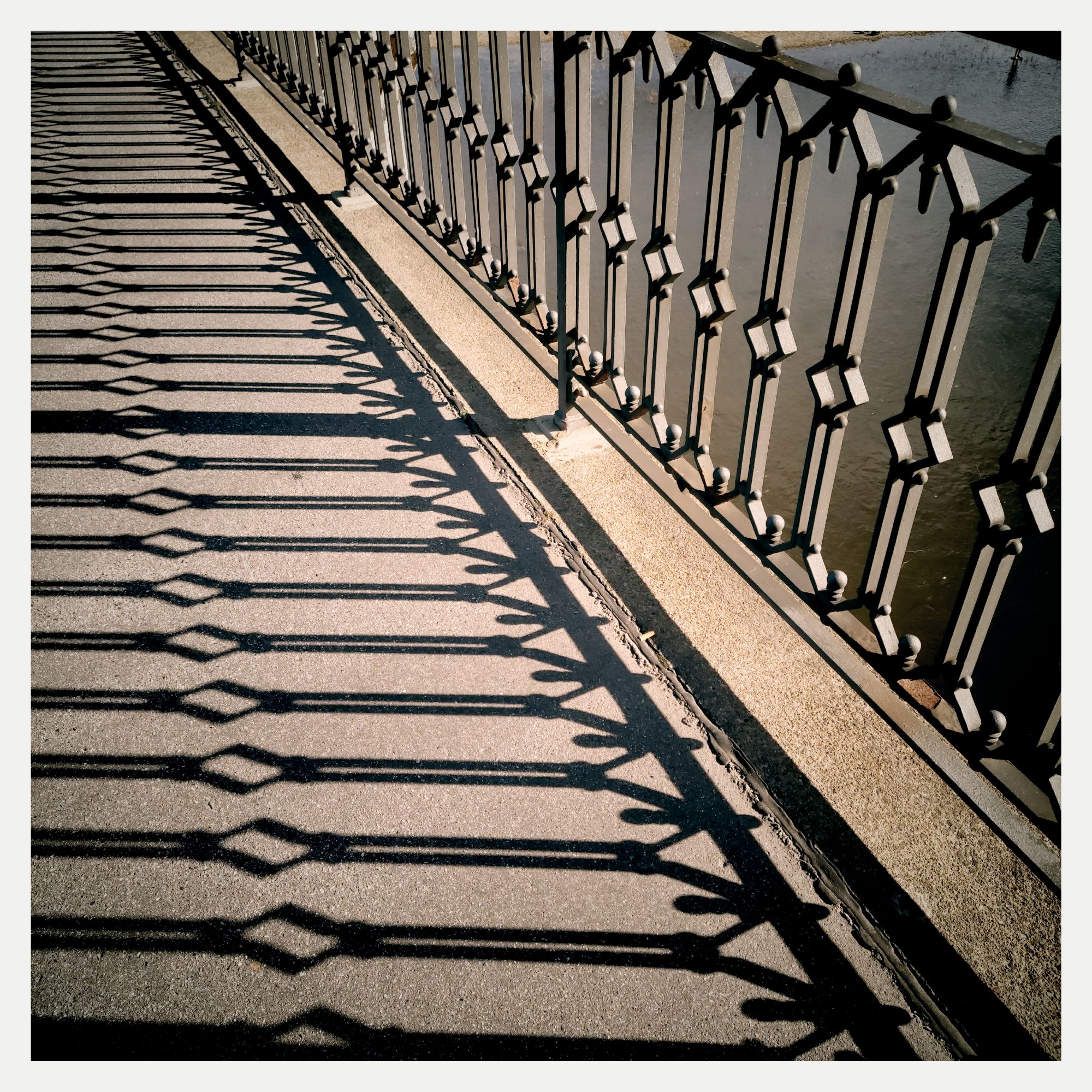 Shadow of a metal railing on a sidewalk.