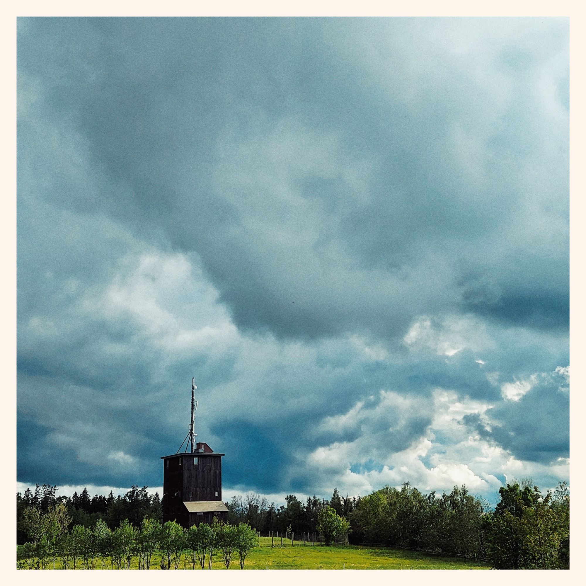 Wild clouds above green fields. A transmission and weather station in between. 